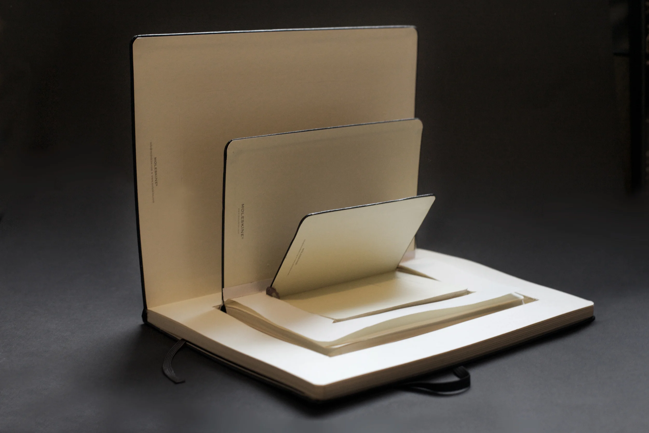 Open notebook with several beige folders inserted into the pages, set against a dark background.