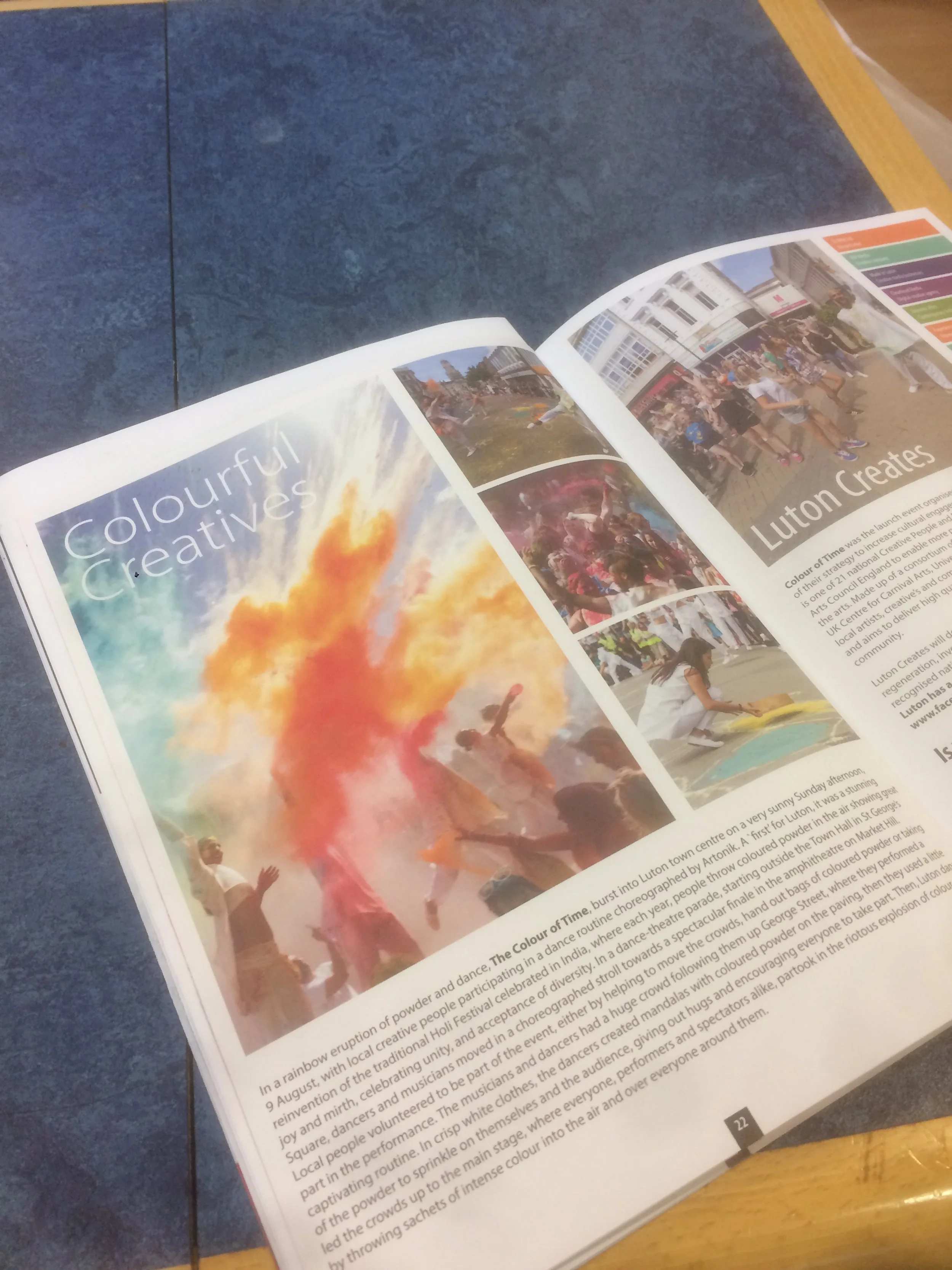 Open magazine pages showing images and text about colorful creative events in Luton, including photos of a powder explosion and outdoor gatherings.
