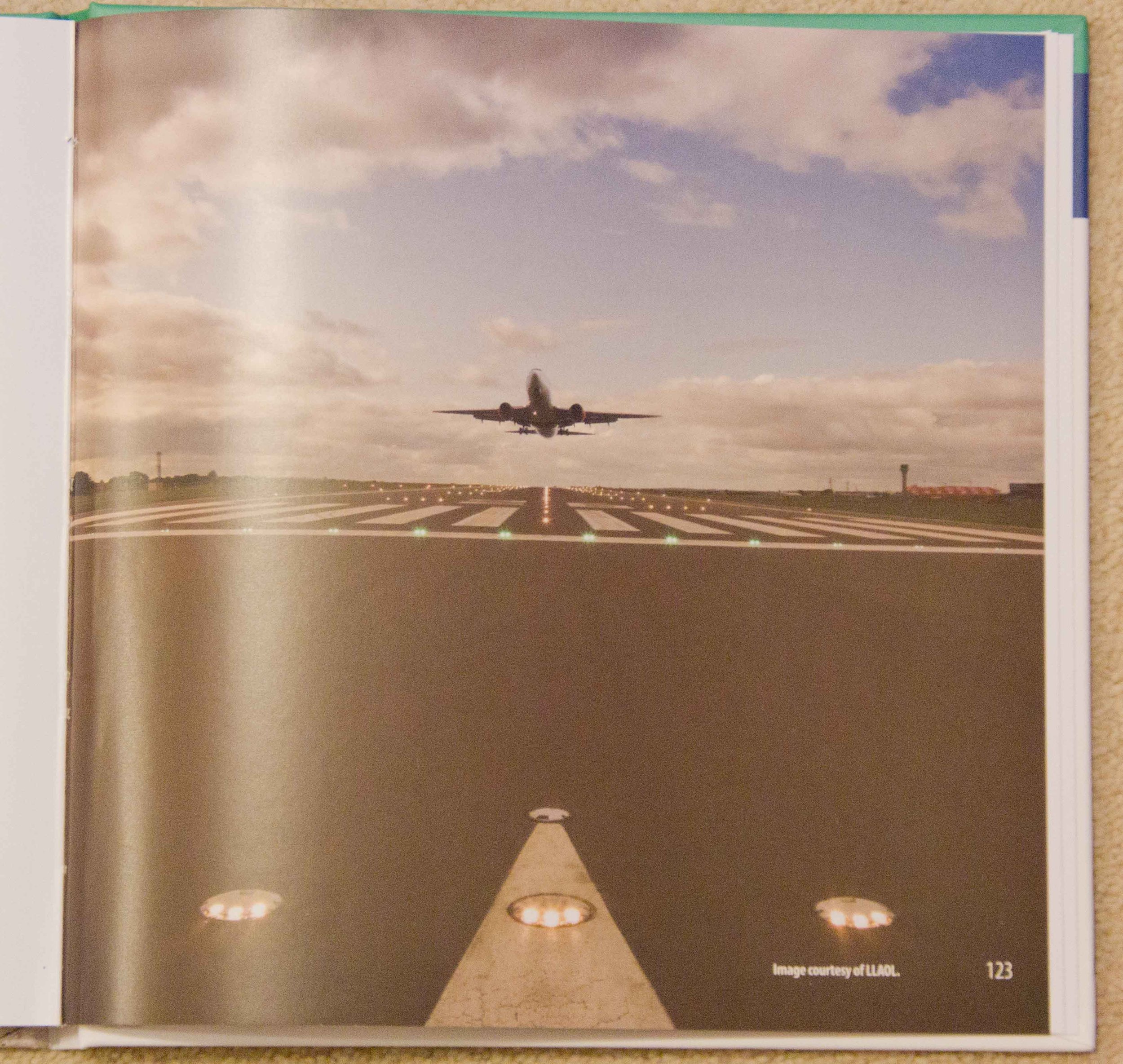 An airplane taking off from a runway with runway lights and a cloudy sky in the background.