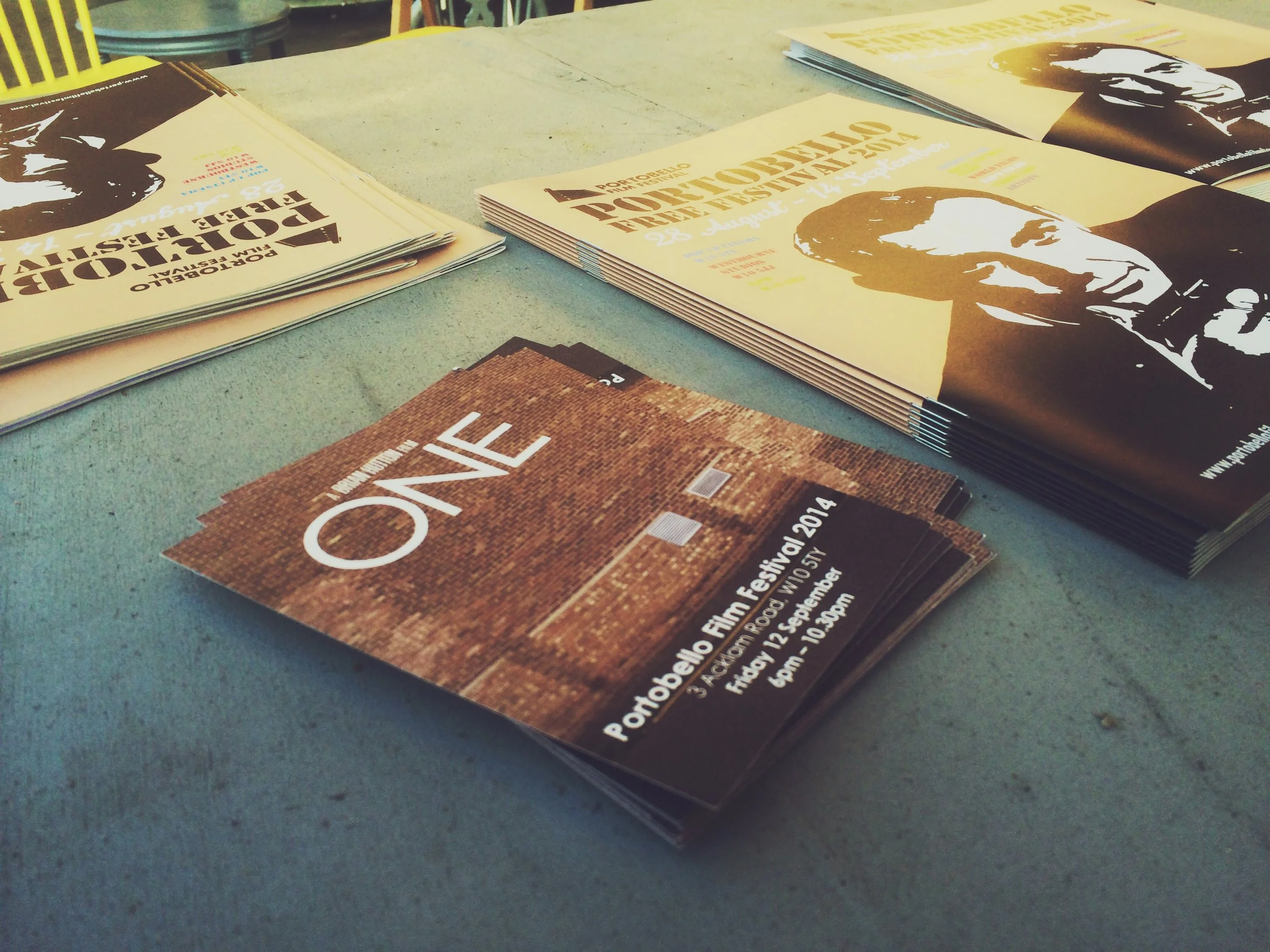 Flyers and brochures for events including Porto Belo Film Festival 2014 and a political event with a man in a suit. The brochures are arranged on a gray surface.