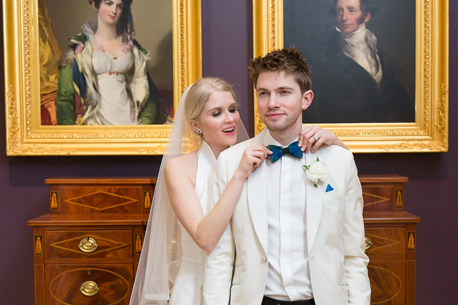 bride adjusting grooms bowtie in front of Charleton art