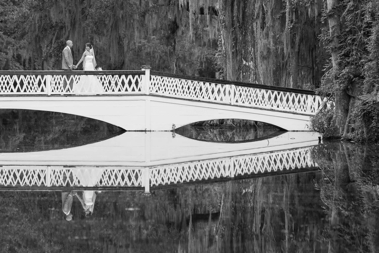 bride and groom walking over iconic bridge with water reflection at Magnolia
