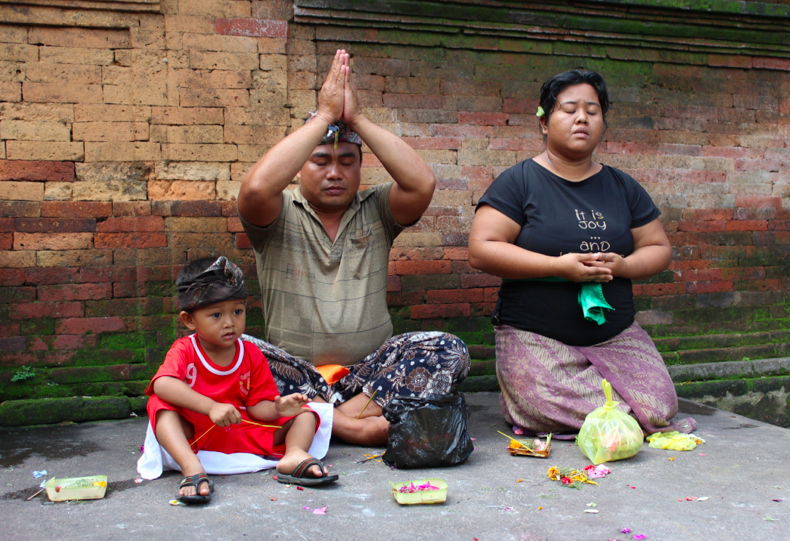 A sarong-clad family praying and leaving offerings