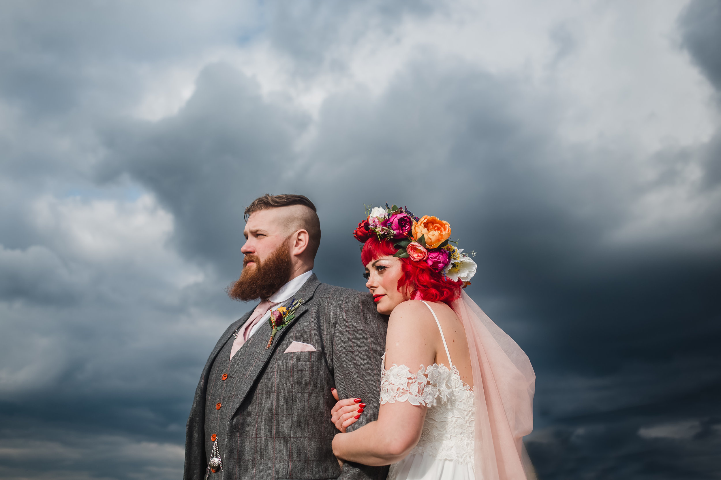 An alternative bride and groom cuddle up under a grey sky outside the Compasses at Pattiswick