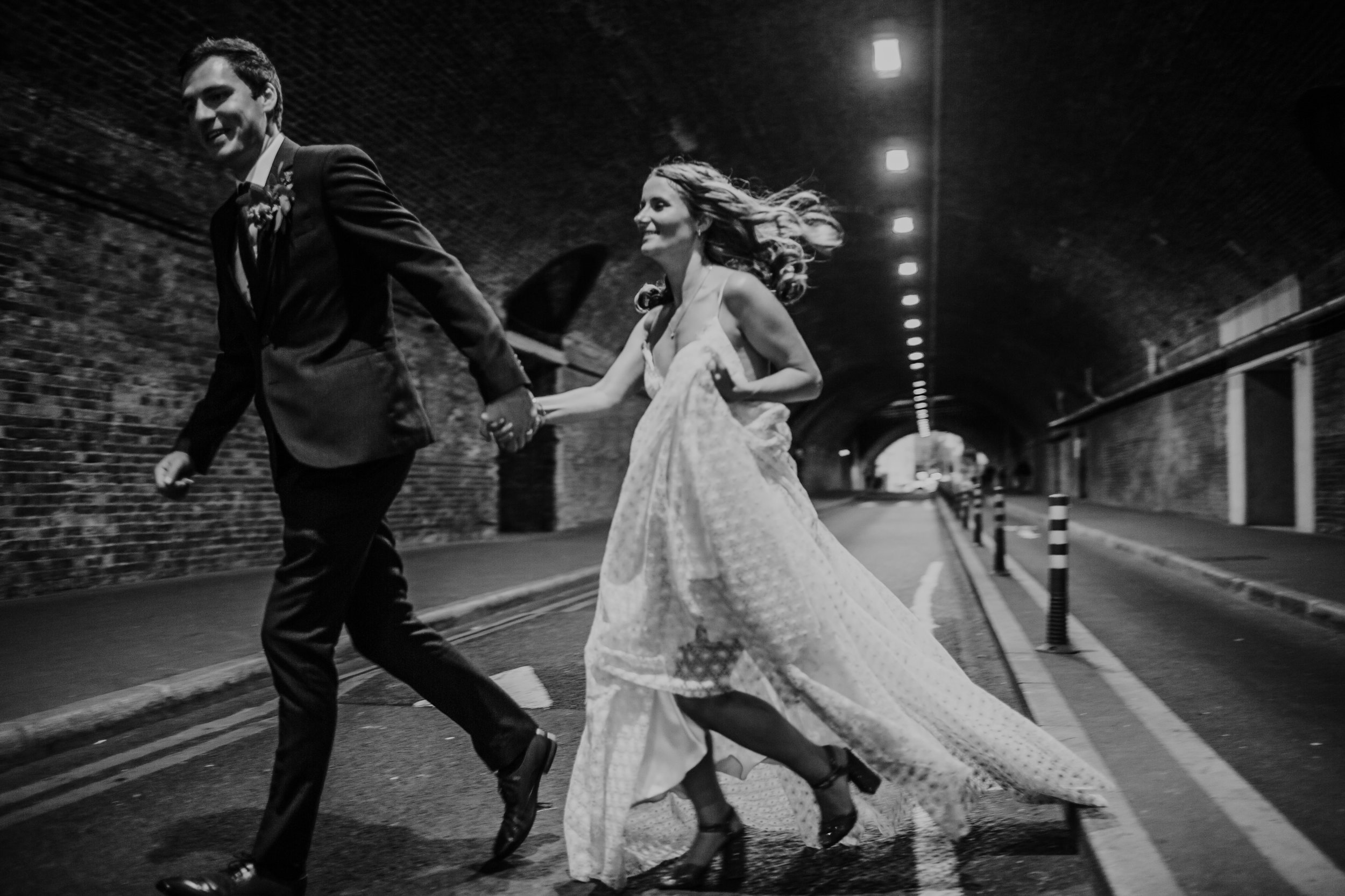 A bride and groom run through a tunnel outside the Taner Warehouse London