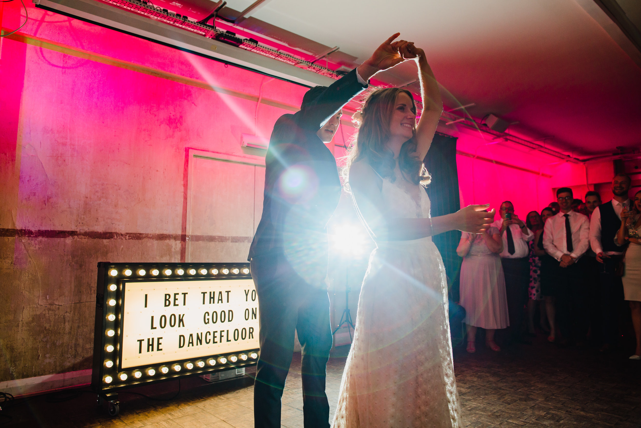 A bride and groom dance in front of a light up sign in Tanner Warehouse London