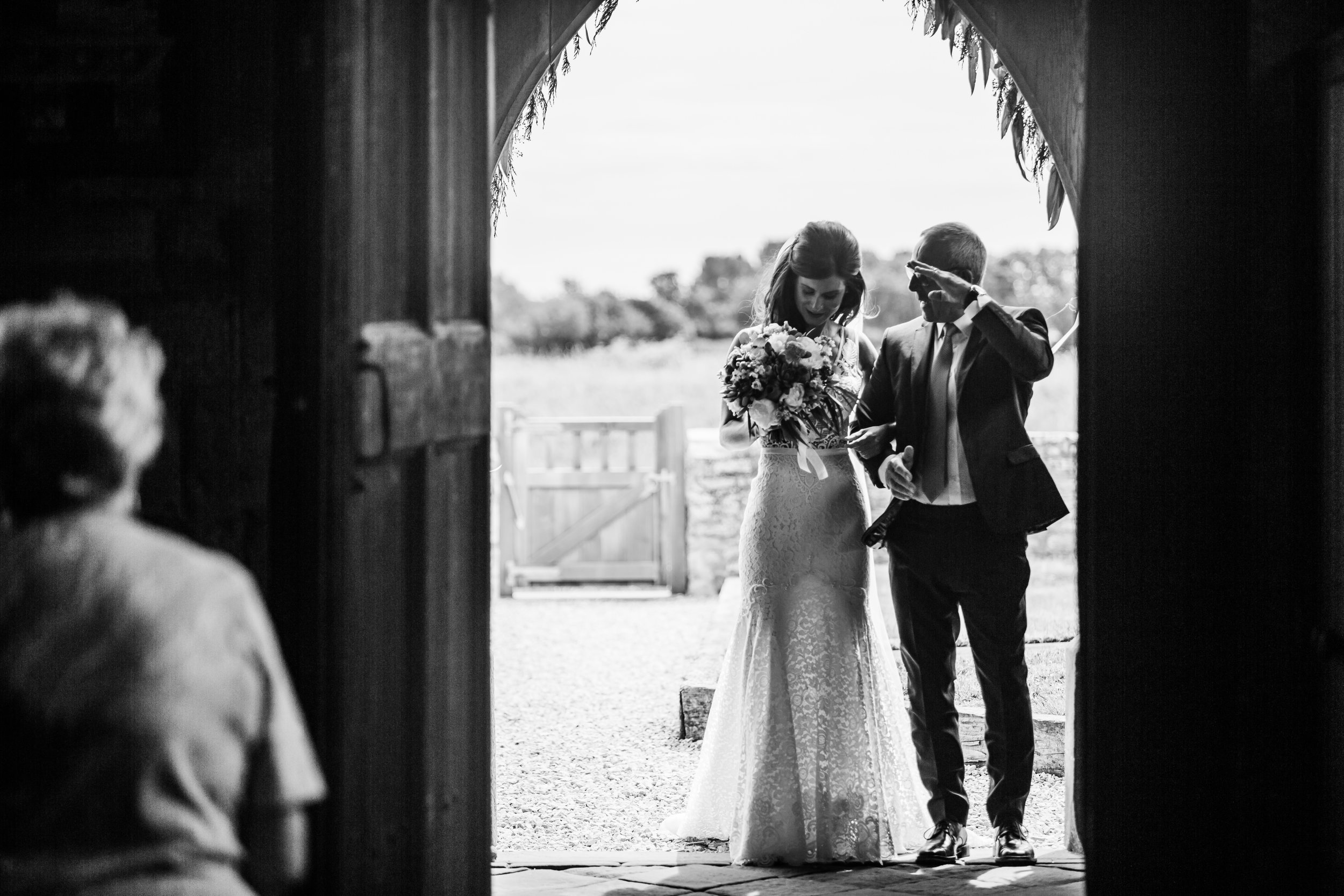 A bride waits with her dad in the entrance of a church. 