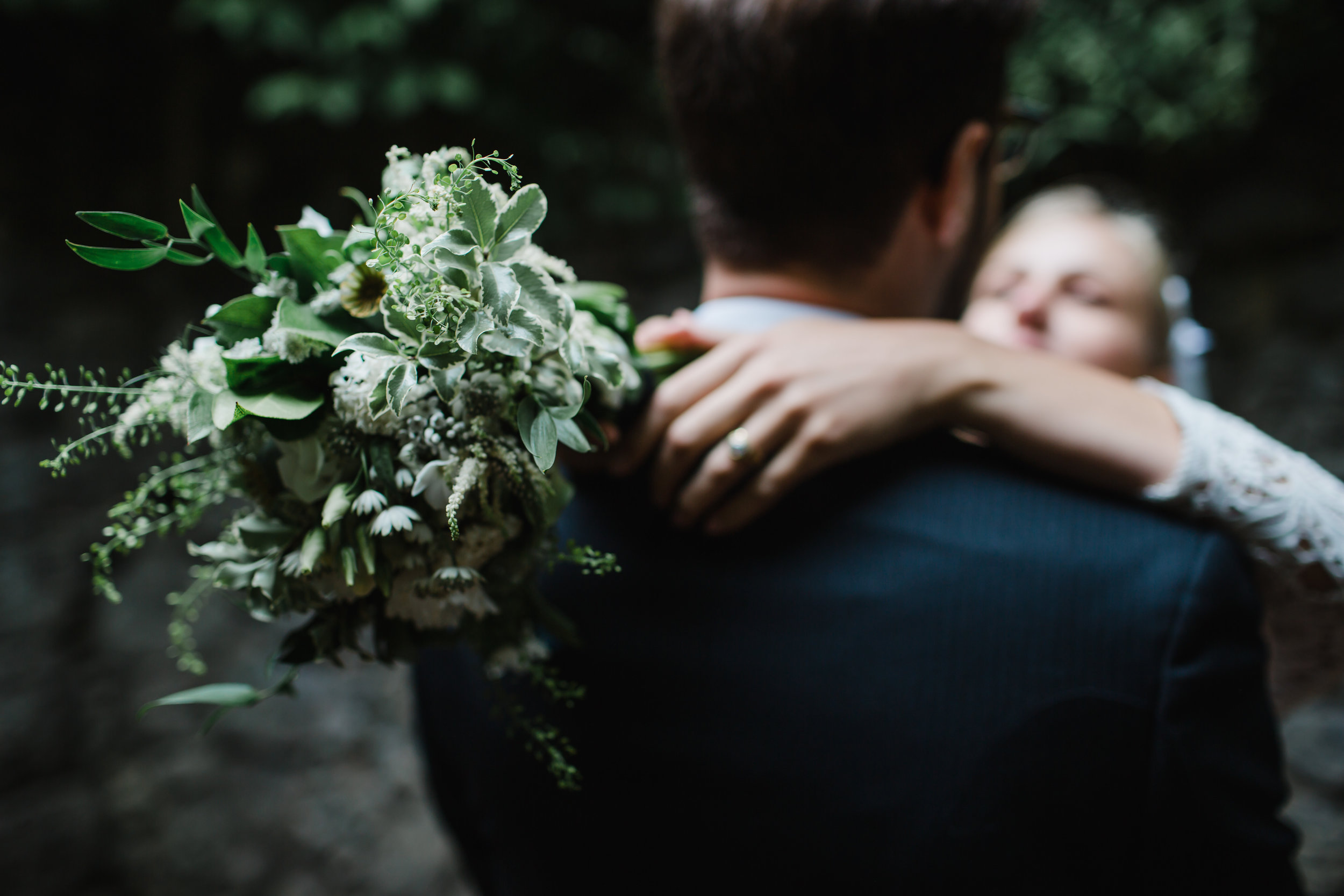 a bride and groom cuddle after a wedding.the bride is holding flowers