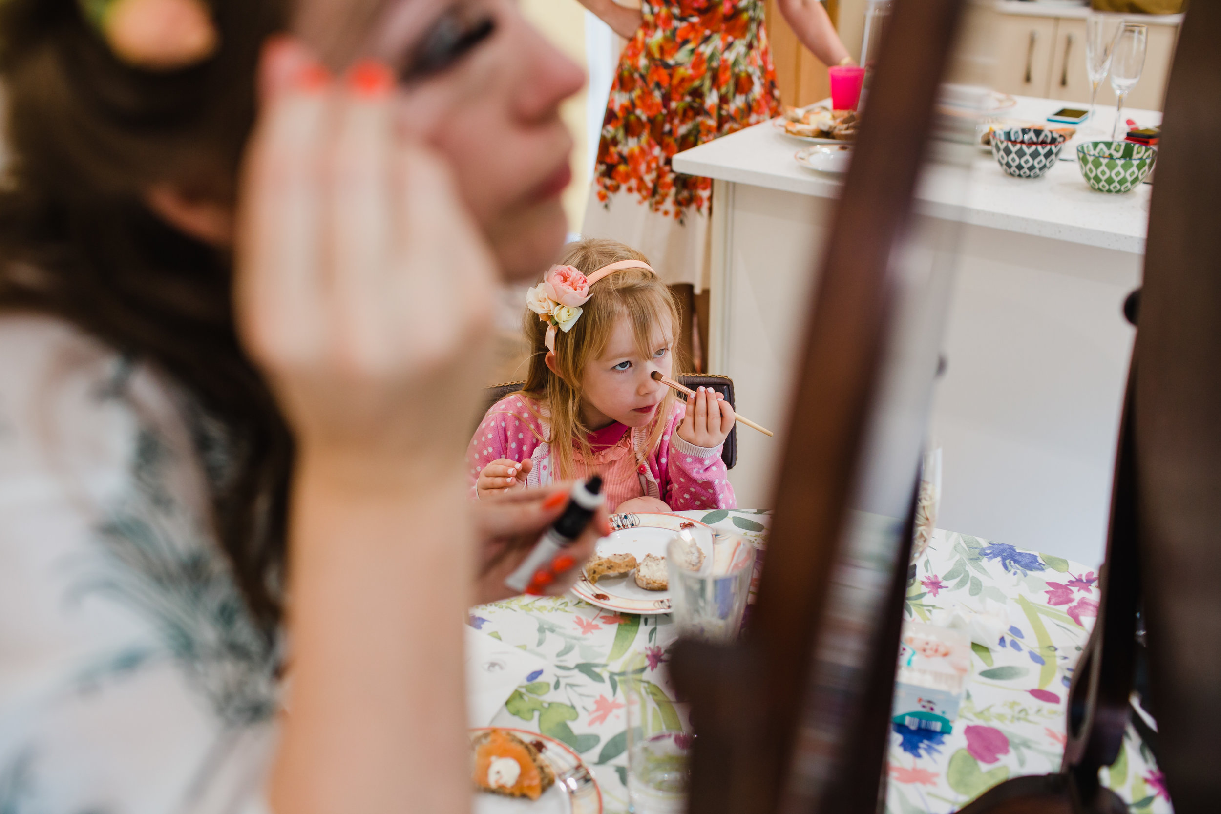 a flower girl copies the bride while putting on make up