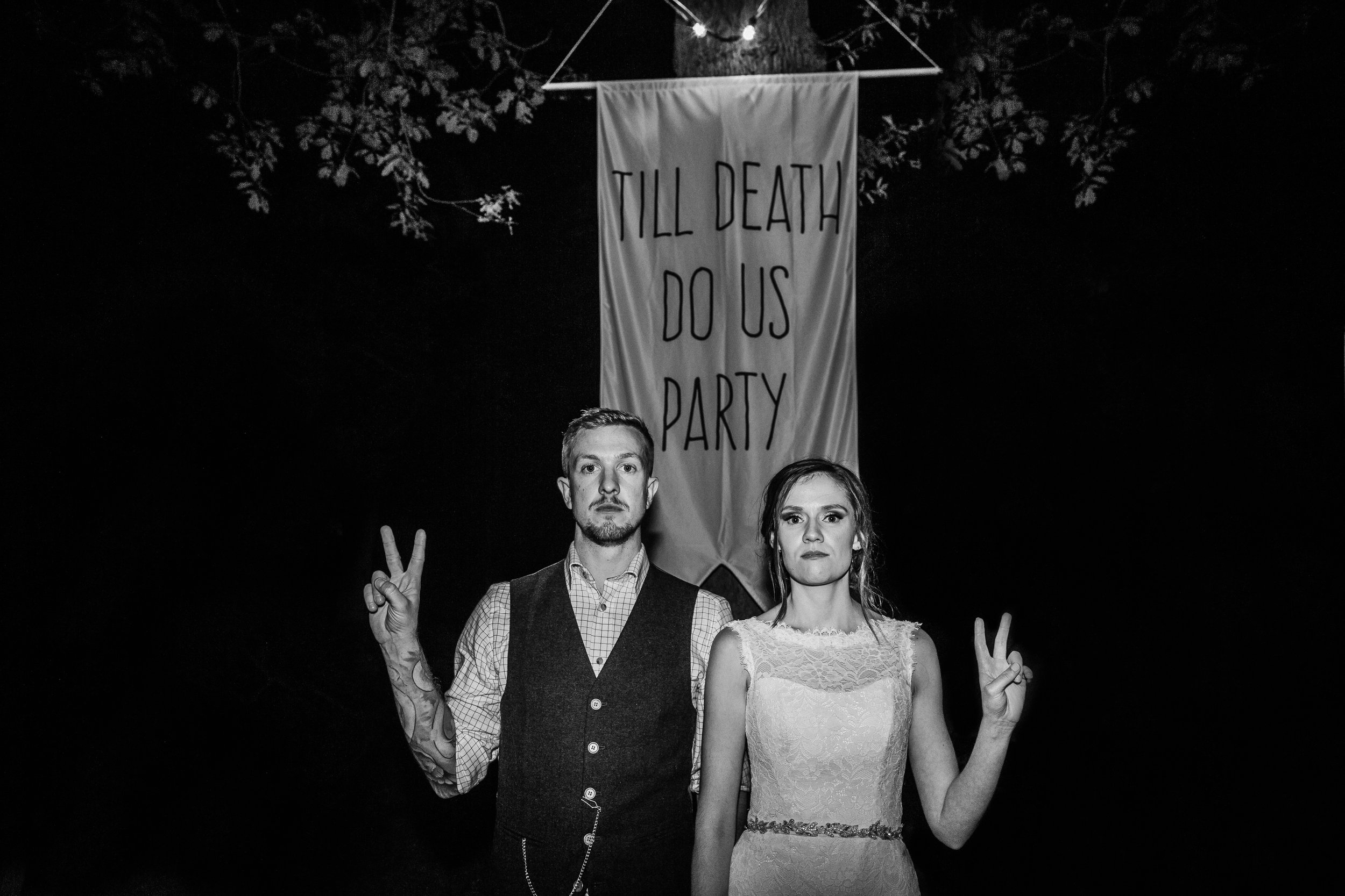 a bride and groom posing in front of a banner saying till death do we party at Enchanted weddings birmingham