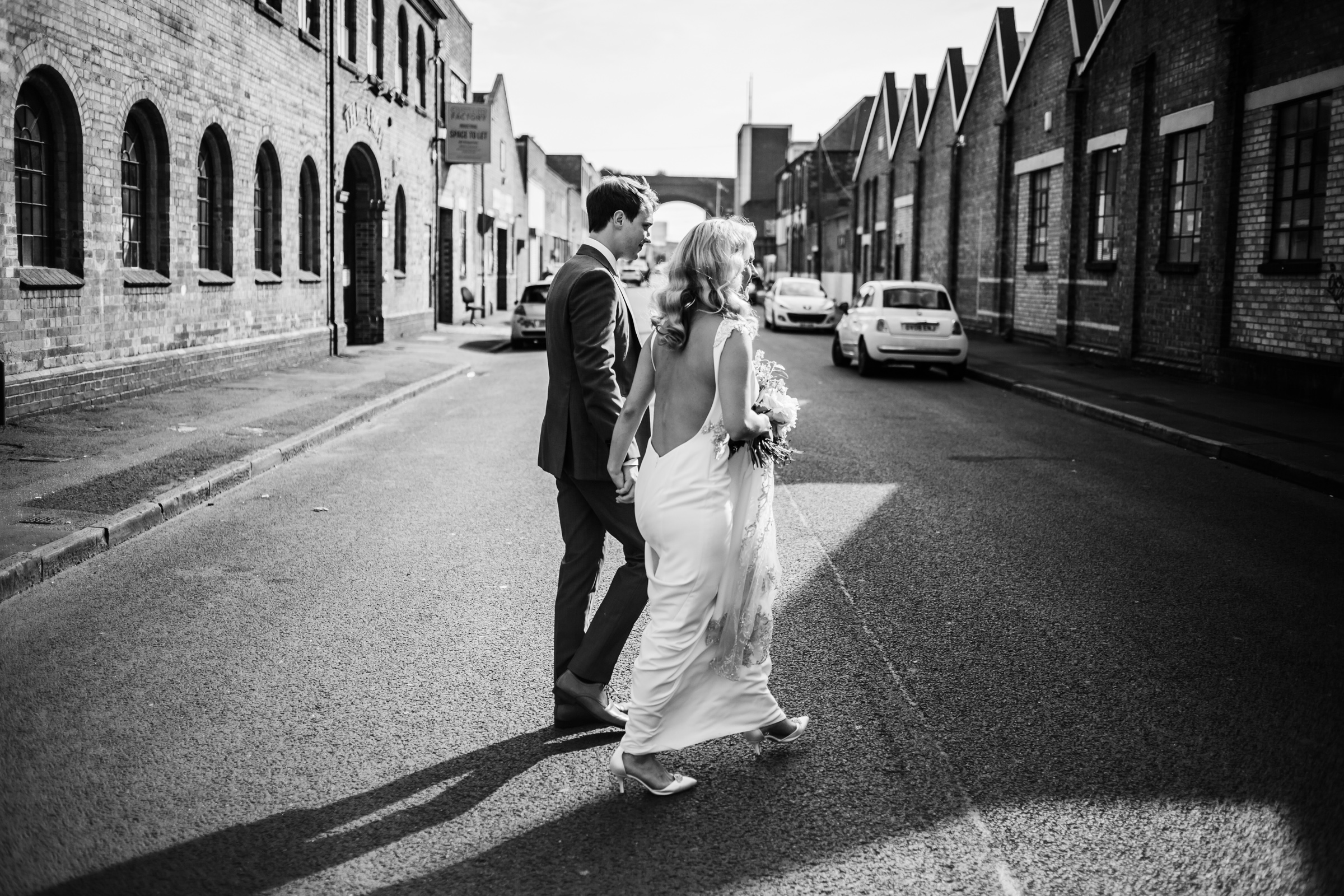 a bride and groom walk through the streets of digbeth
