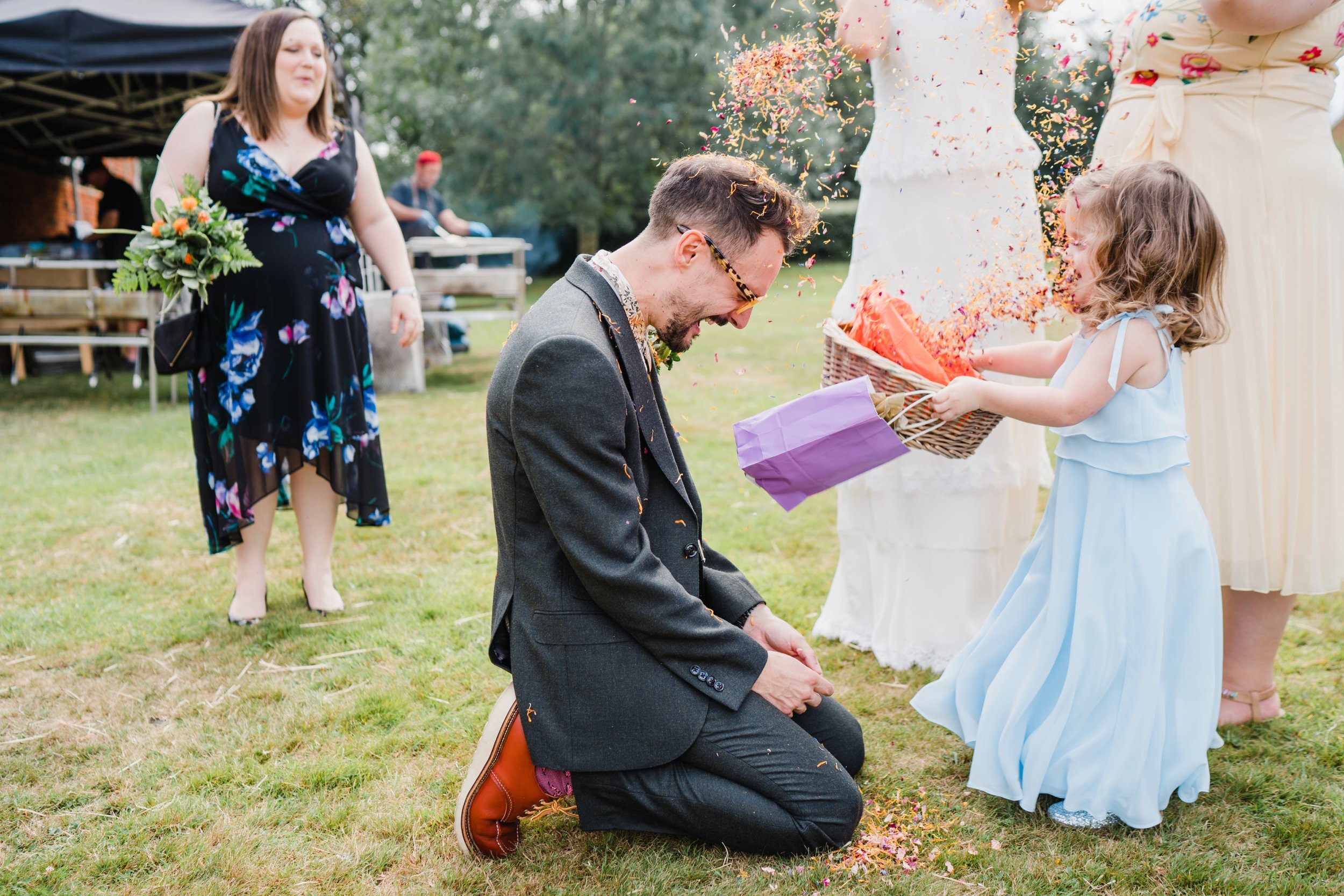 a flower girl throws confetti at the groom