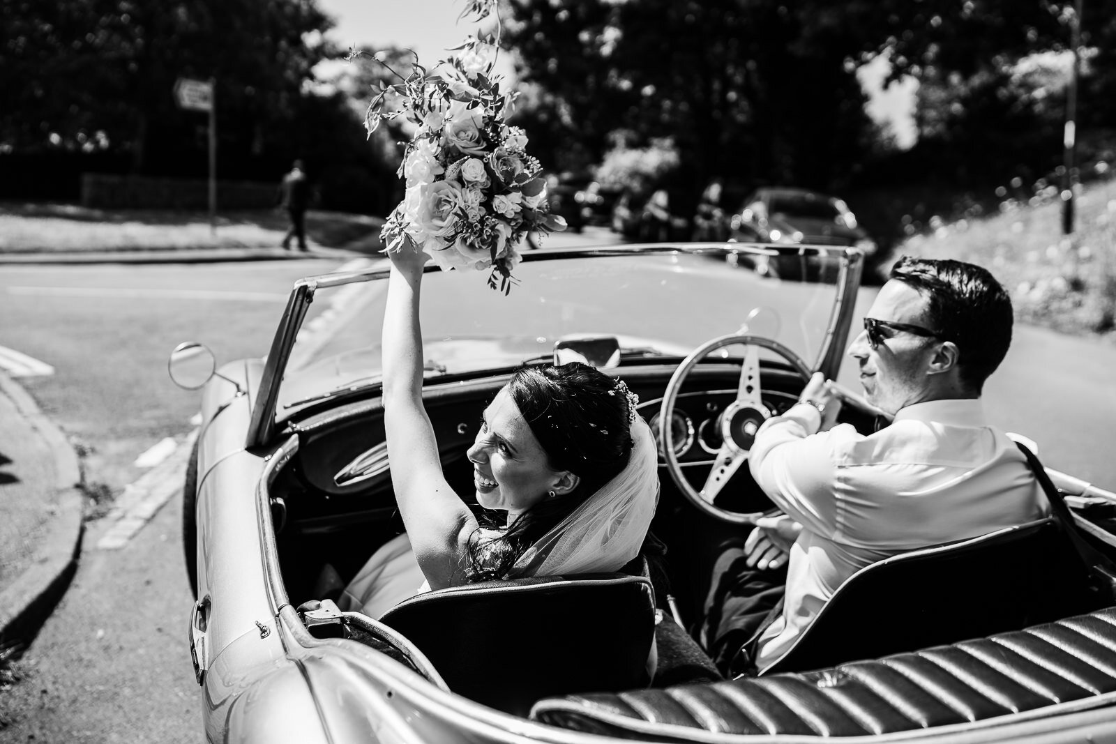 A bride and groom leave the church in a convertible car. 