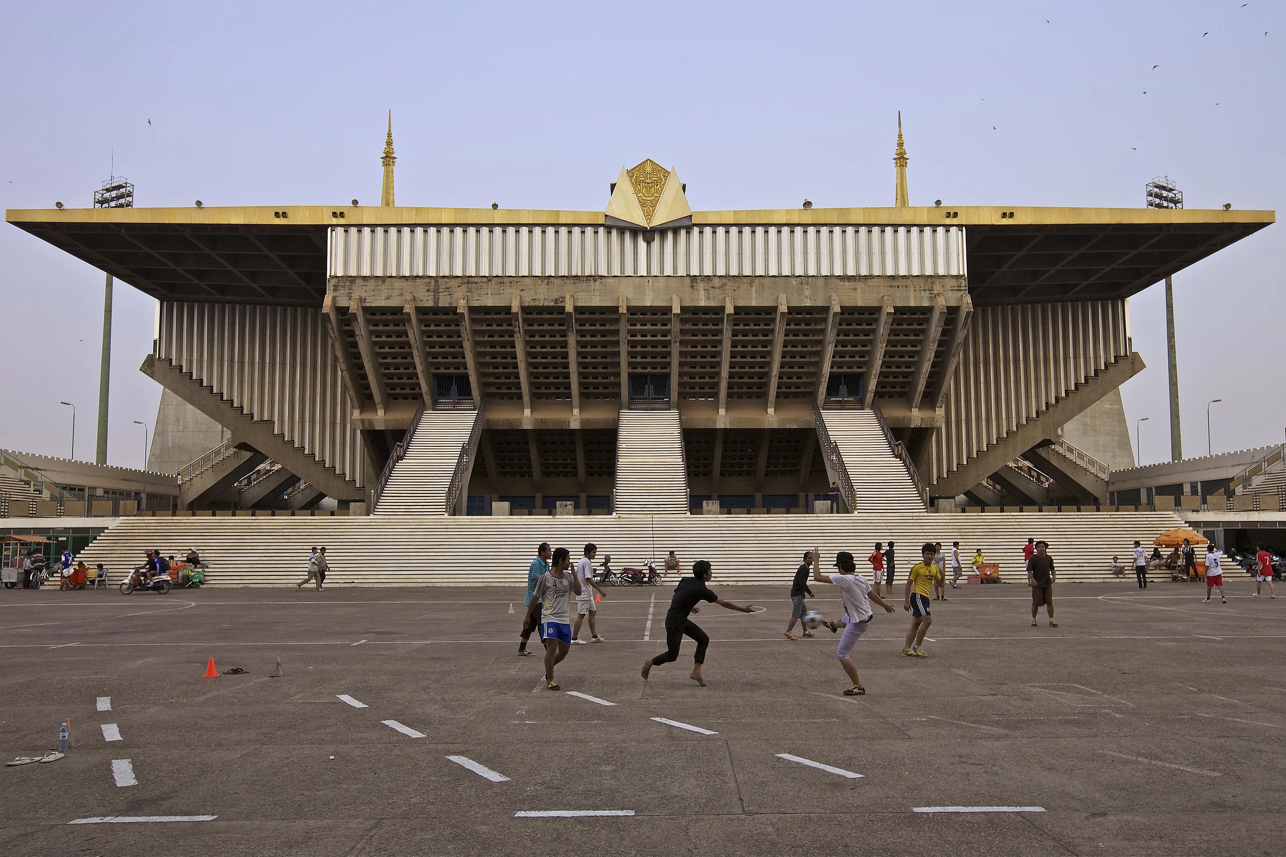 a football game in front of the olympic stadium - part of phnom pen's national sports complex and prime example of modern khmer architecture built by local architect vann molyvann. the stadium was never used for the intended occasion of hosting the 1963 southeast asian peninsular games. during the early days of the khmer rouge occupation, citizens of phnom penh were ordered to gather at the complex before their forced expulsion from the capital city. political executions also took place on the grounds.