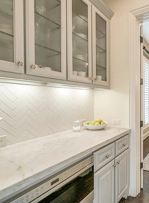 After - updated Butler's pantry with gray cabinets, Taj Mahal quartzite, herringbone tile backsplash and undercounter microwave drawer. - Carla Aston Designer