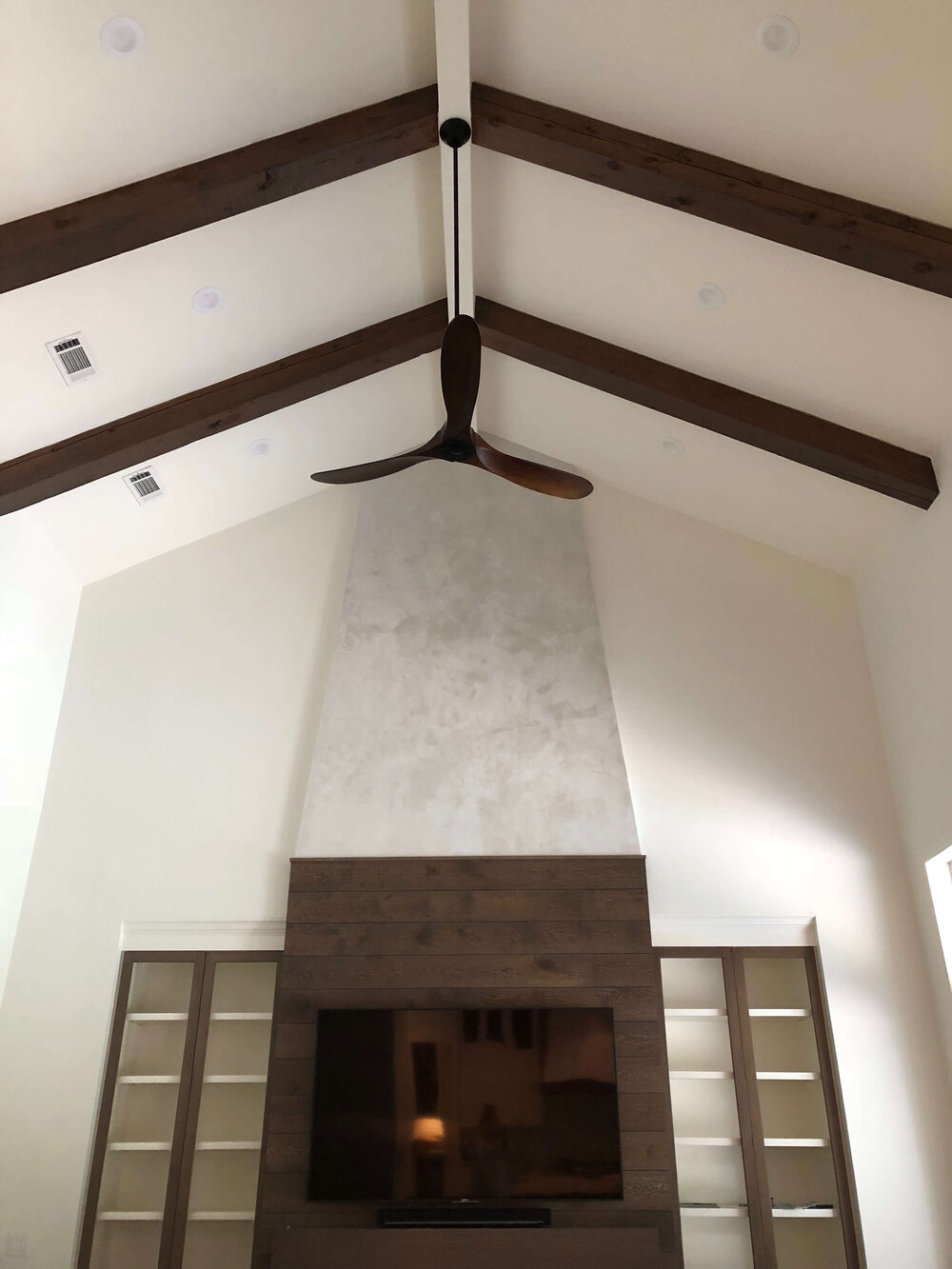 TV mounted over fireplace with wood flooring paneled fireplace wall is camouflaged on top of the dark wood planks. Designer: Carla Aston