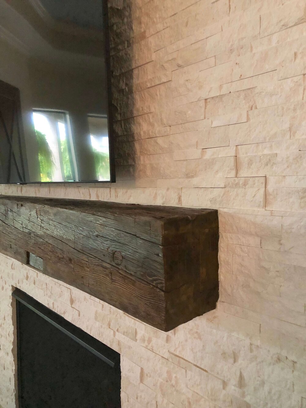 Rustic mantel installed at fireplace wall with light, neutral stacked stone cladding.