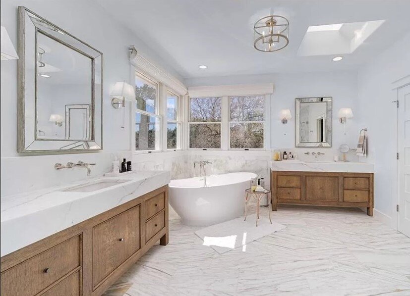 AFTER  - This white marble bathroom with a free standing tub and wood cabinetry enhances this home’s custom look. carlaaston.com