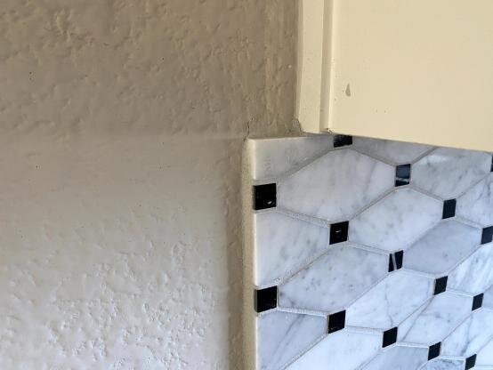 Tile backsplash gone too far - not aligning with the upper cabinet. The unfinished edge is unappealing and feels incomplete too.