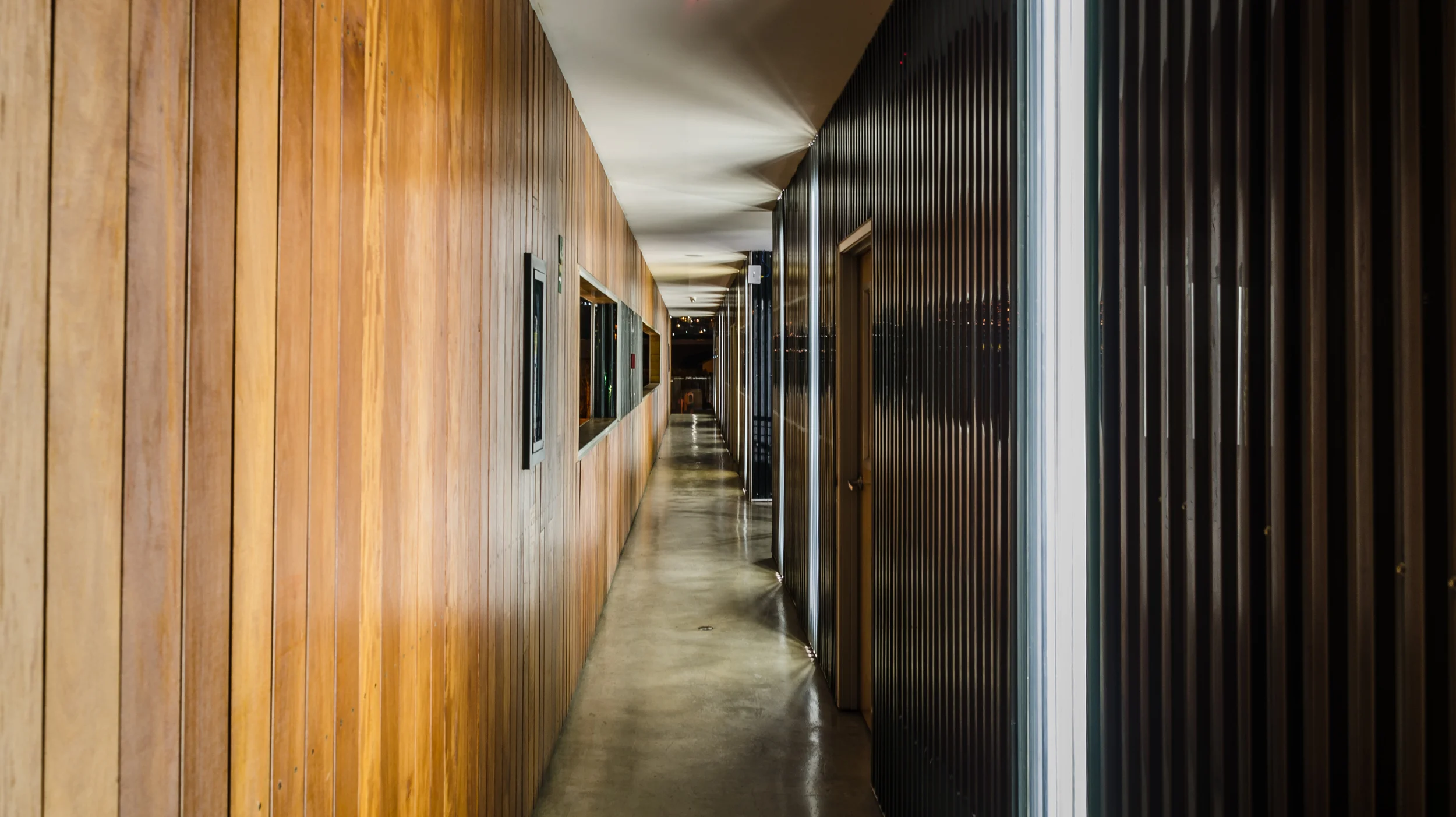 Modern corridor with wooden and metal walls, polished concrete floor, and overhead lighting.