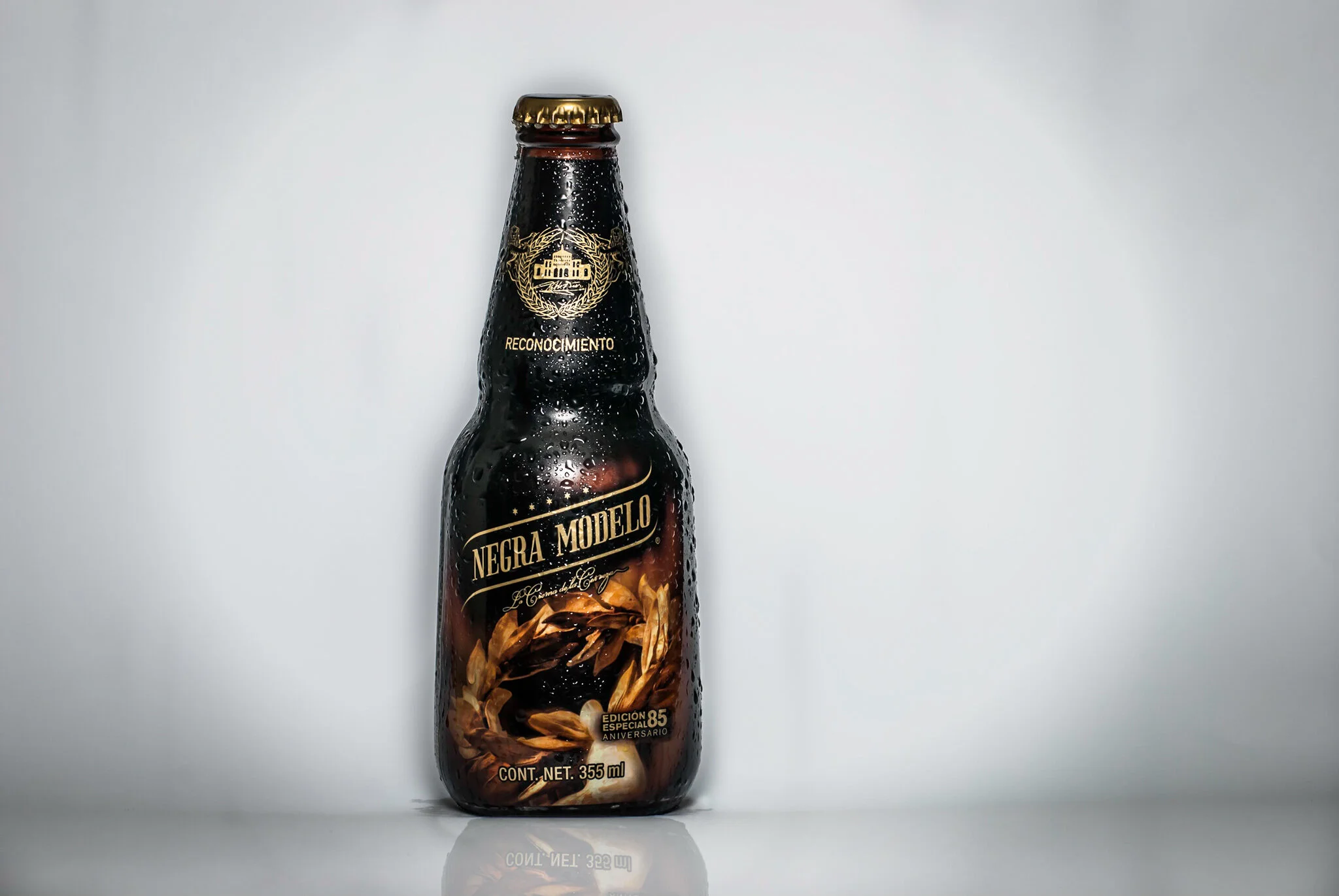 A dark glass bottle of Negra Modelo beer with condensation, placed on a reflective surface against a plain light background.