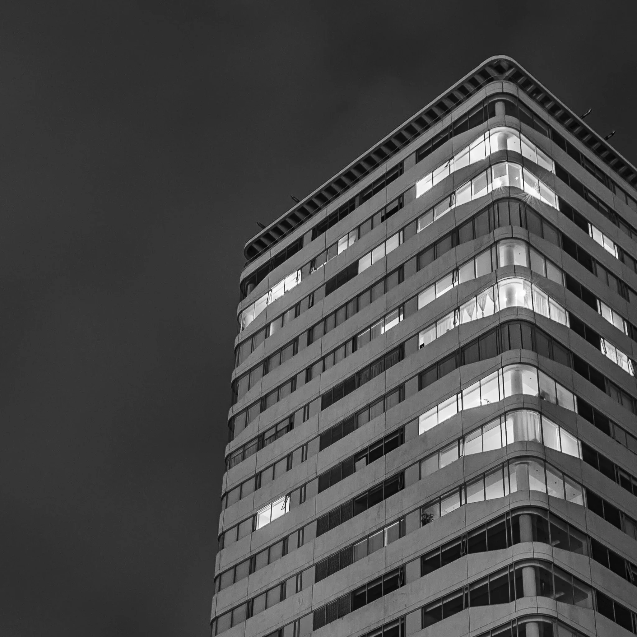 Black and white photo of a modern multi-story building with rounded corners and illuminated windows at night.