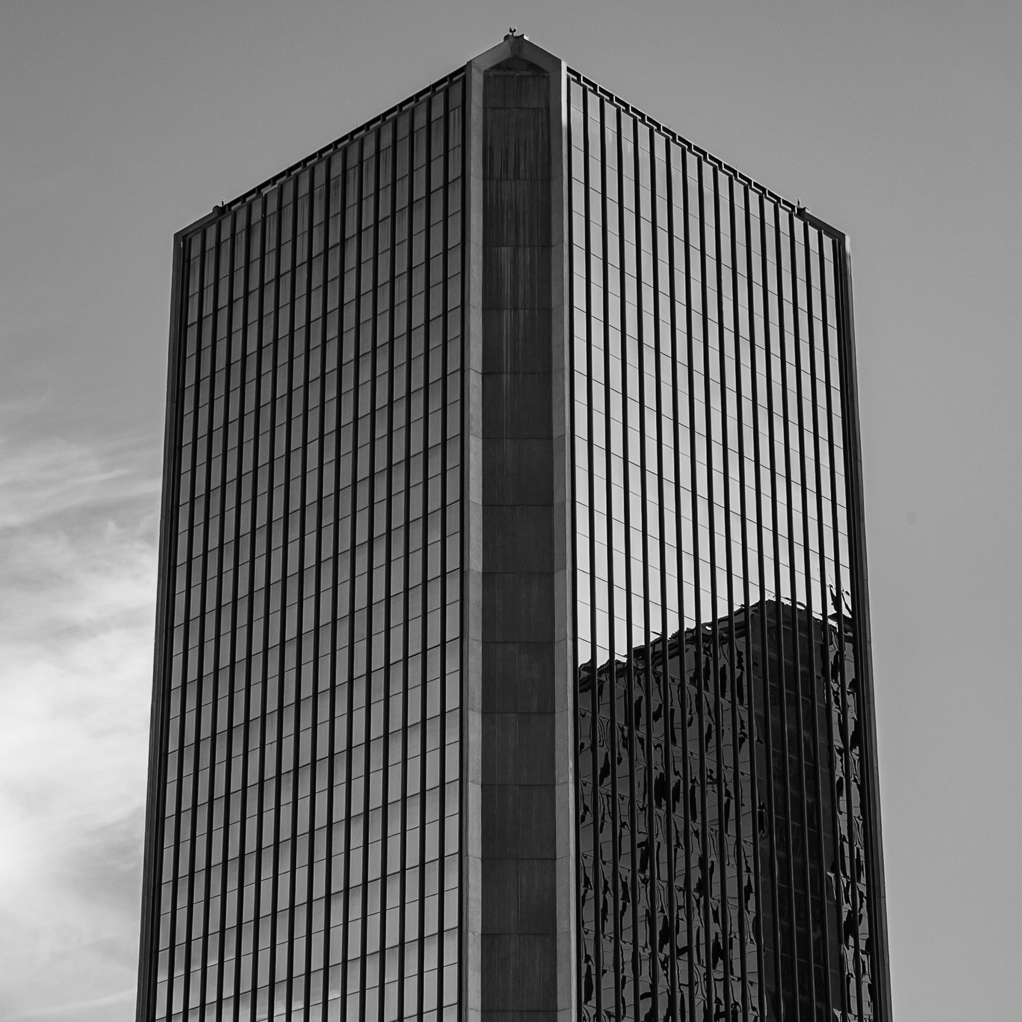 A tall, modern office building with a glass facade reflecting the surrounding structures, captured in black and white.