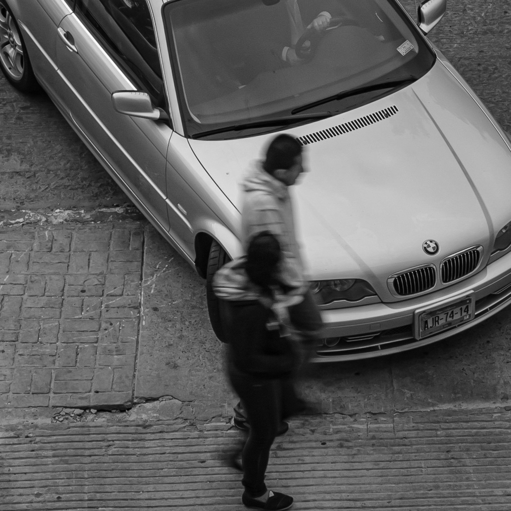 A silver BMW car parked on the street with a person walking past in the foreground.