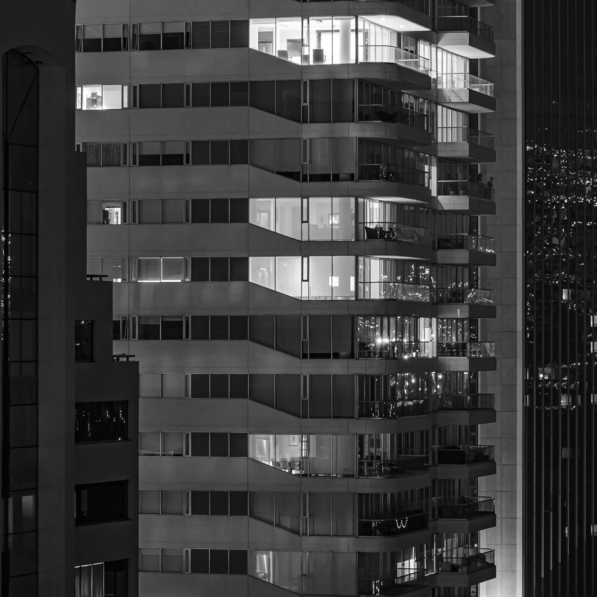 Night view of a modern high-rise apartment building with illuminated windows and some balconies visible in the black and white photo.