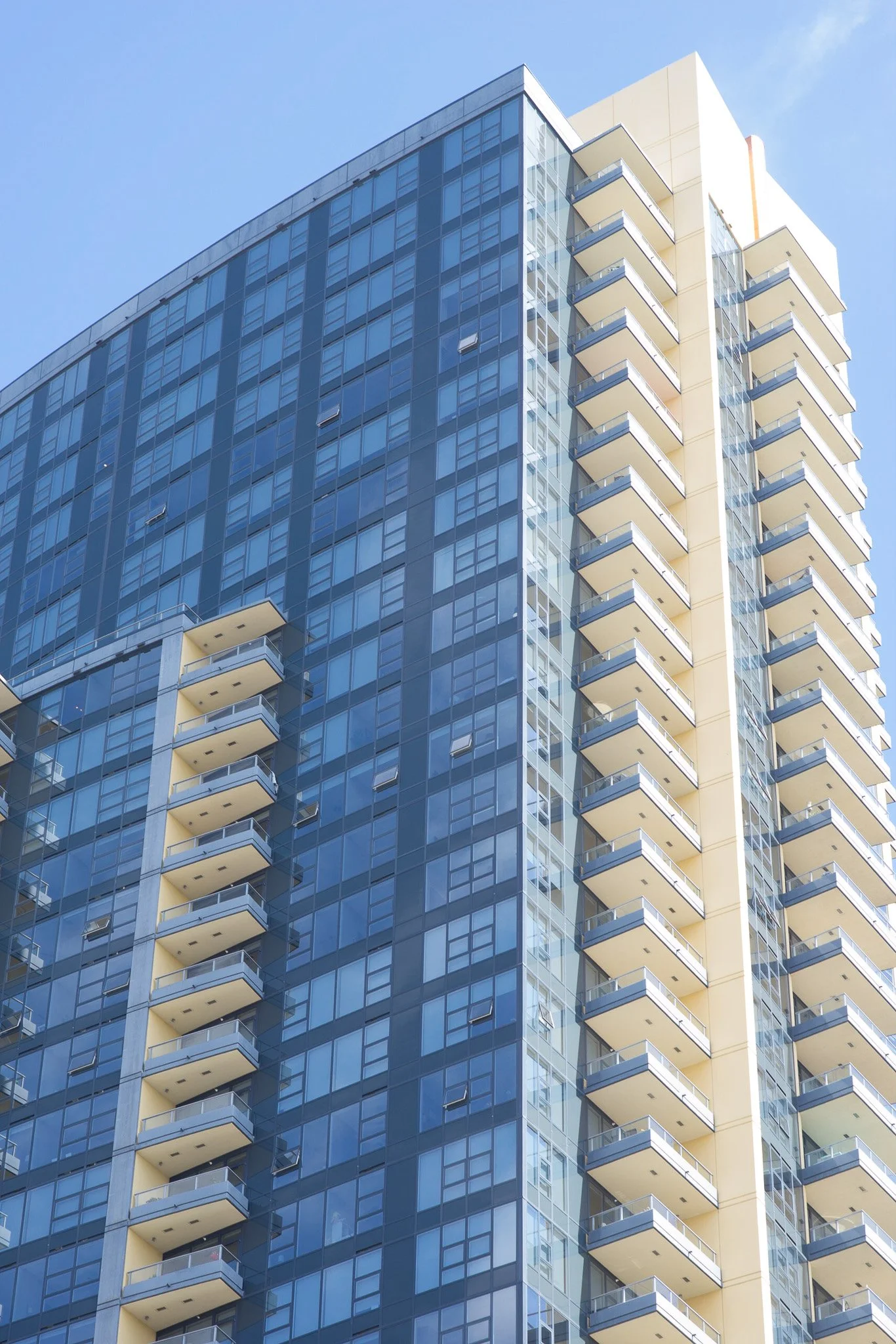 Modern high-rise building with glass windows and balconies against a blue sky.