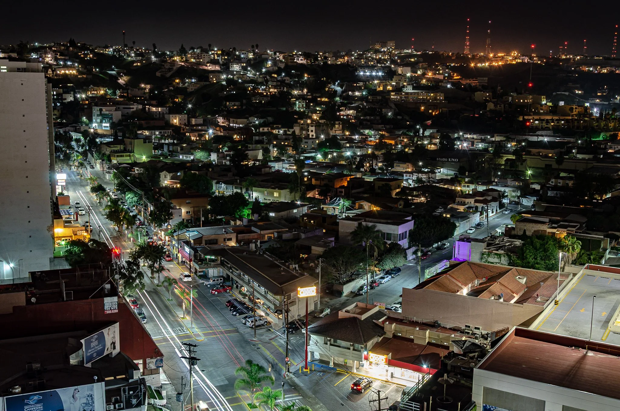 Nighttime cityscape with illuminated streets, buildings, and parked cars