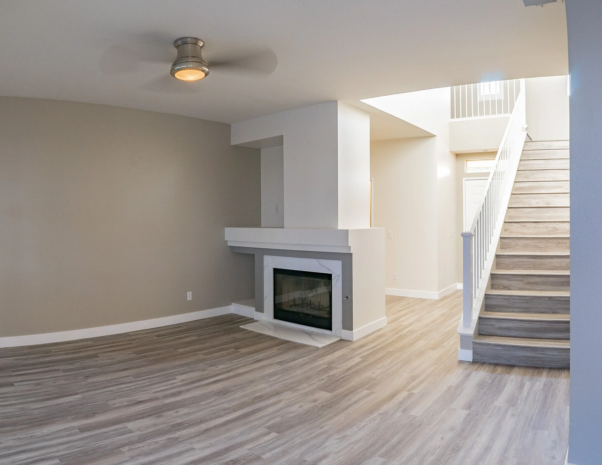 Empty living room with fireplace, staircase, and light wood flooring