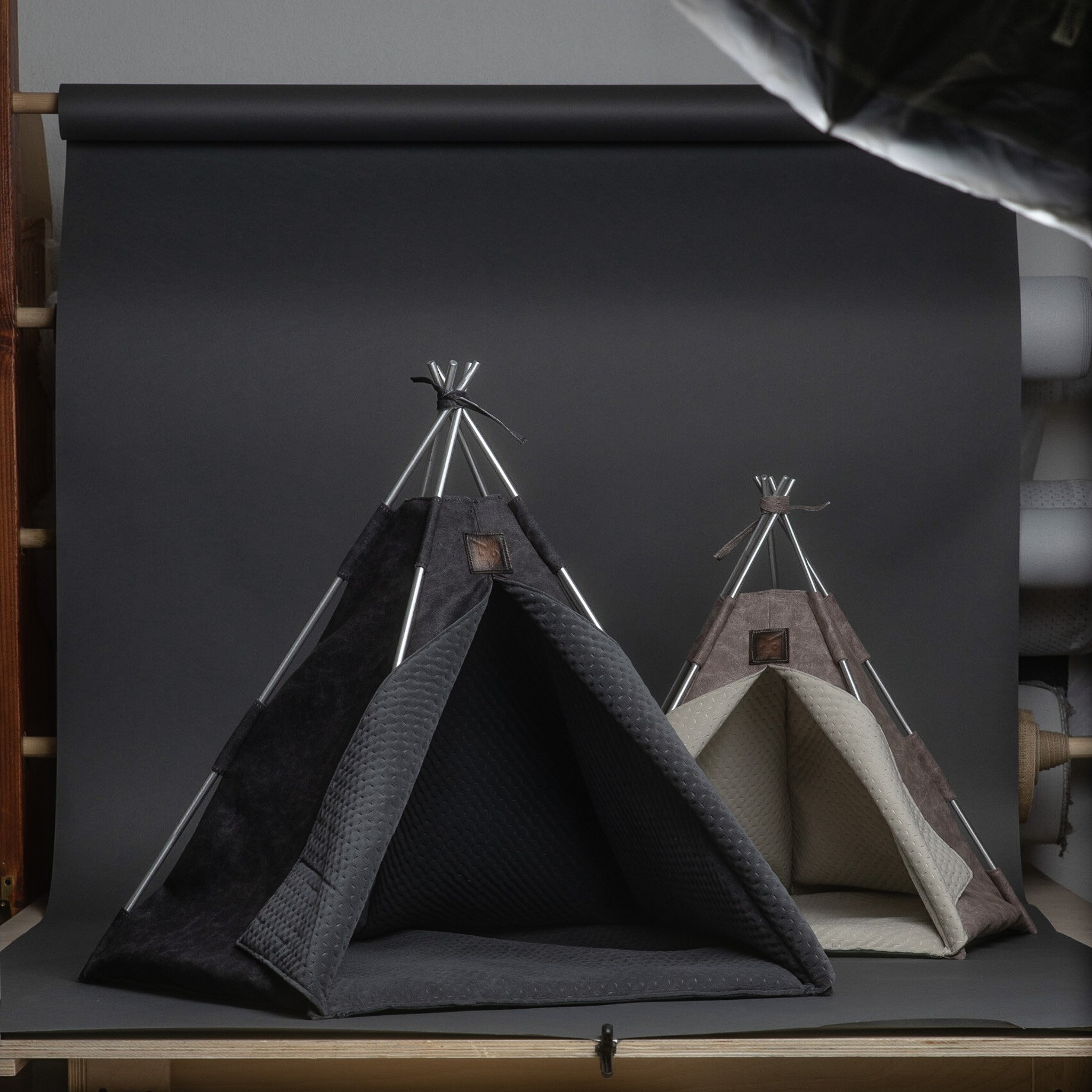 Two pet tents with metal poles, fabric sides, and padded interiors placed on a black surface against a black background.