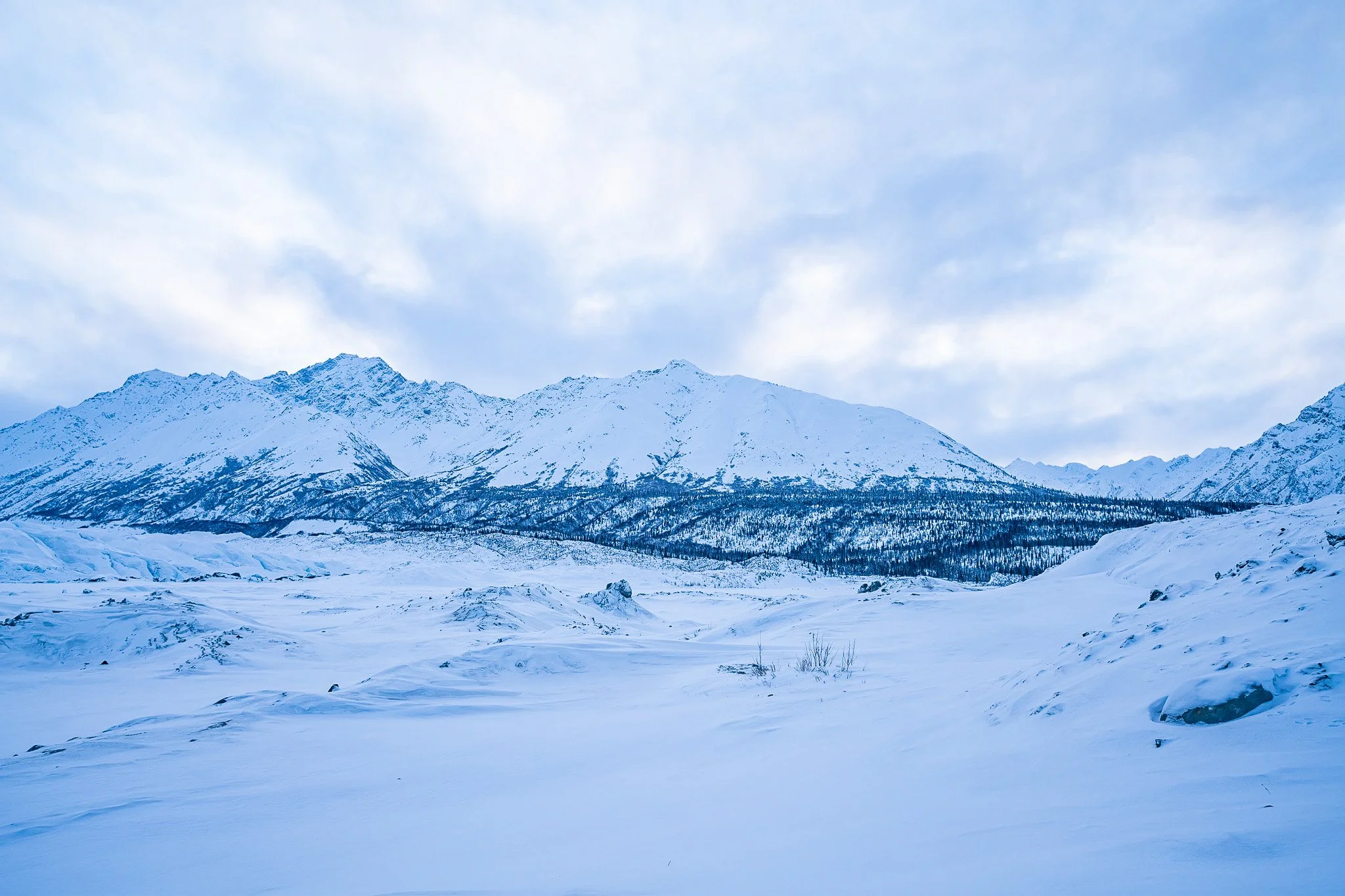 Snow-covered mountains and plains under a partly cloudy sky.