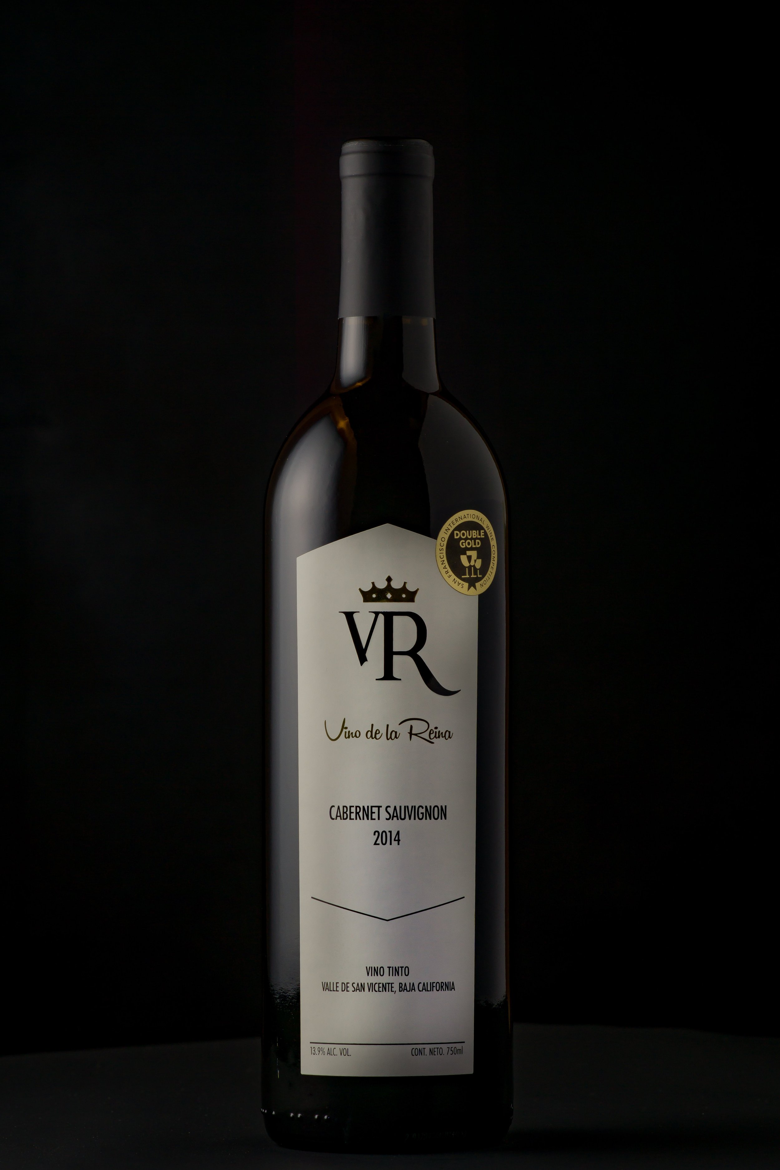 A bottle of VR Uno de la Reina Cabernet Sauvignon 2014 red wine on a dark background with a black cap and a white label.