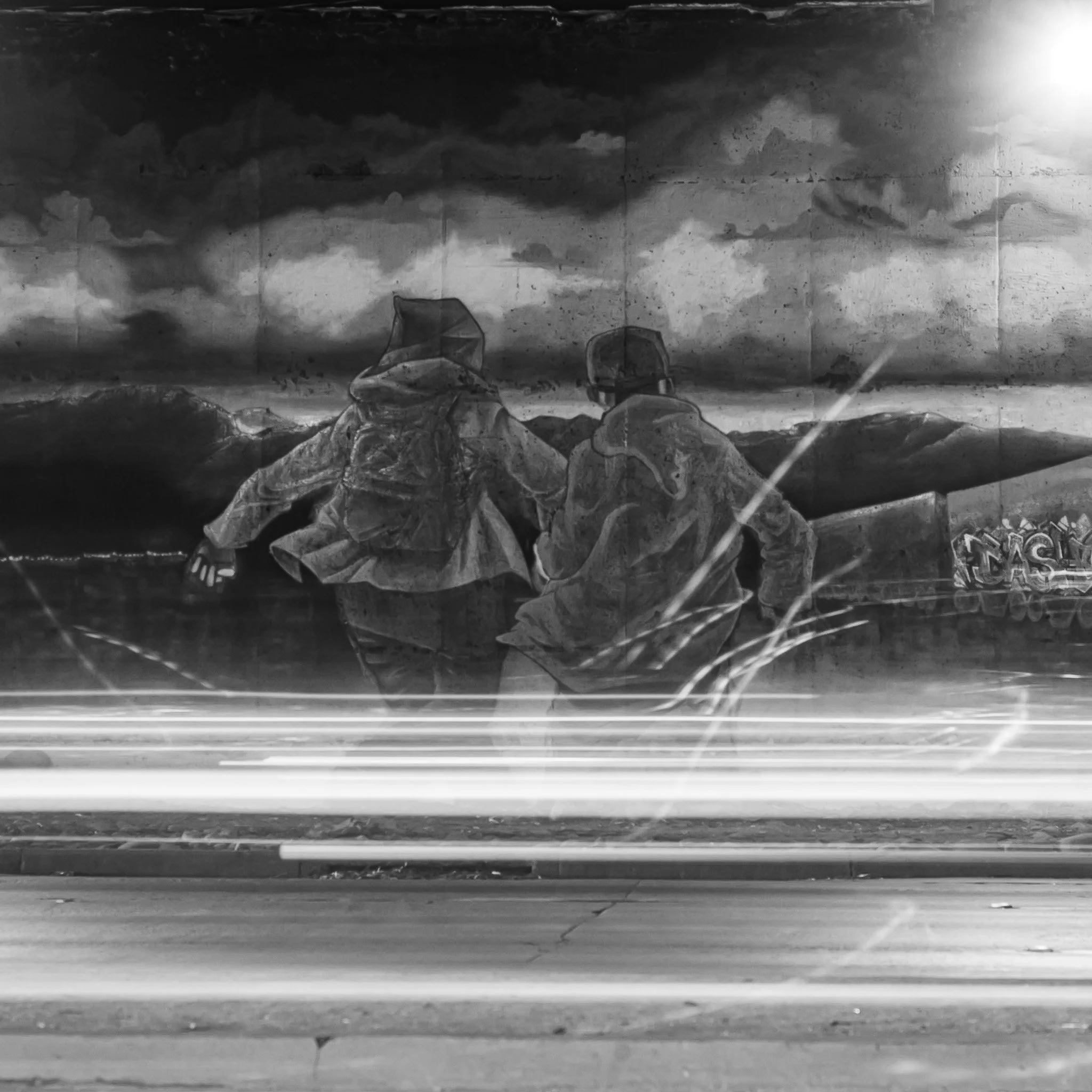 Black and white mural of two people walking, set against a mountain landscape, with light streaks in the foreground.