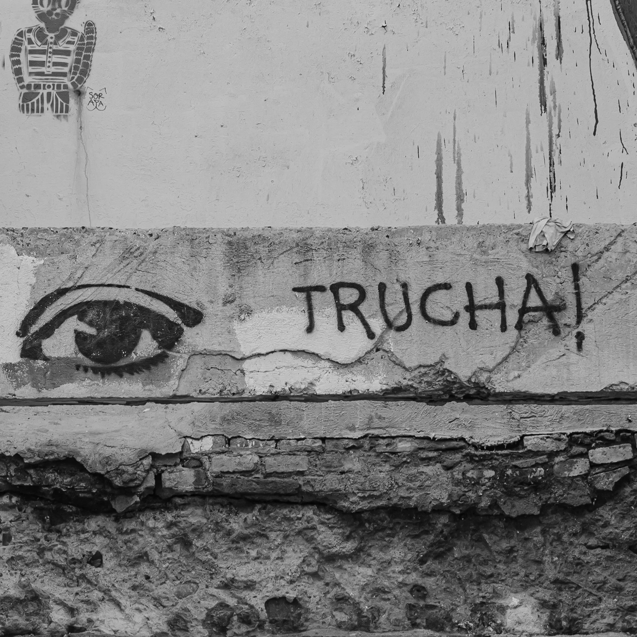Graffiti of an eye next to the word 'TRUCHA' on a cracked wall with weathered textures.