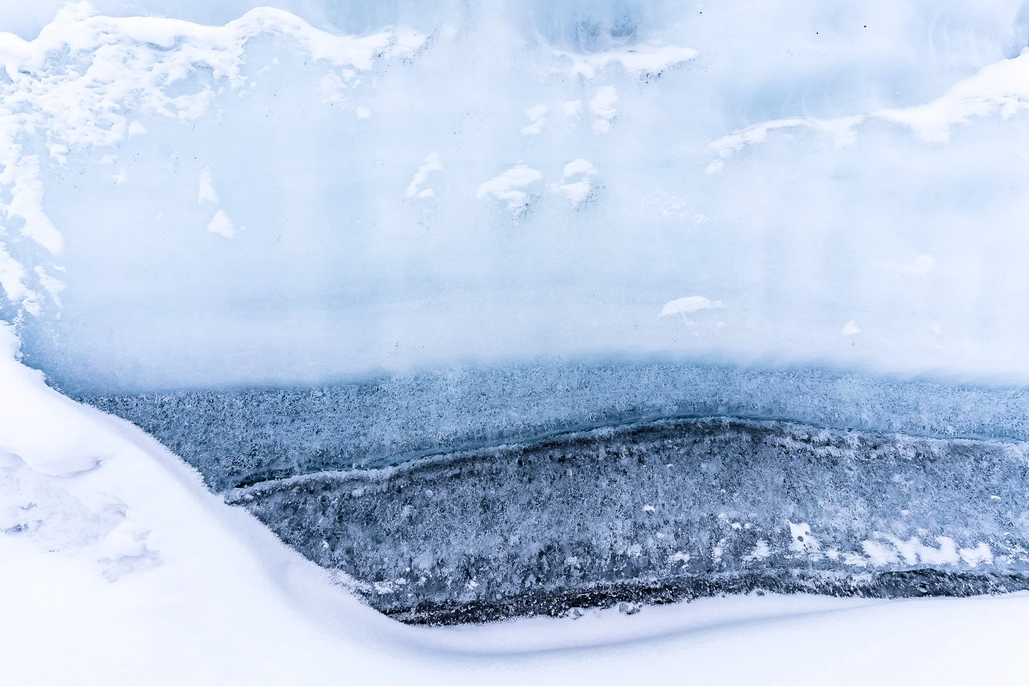 Close-up of an ice cave or glacier with layers of snow and ice, showing a mix of white, blue, and dark ice textures.