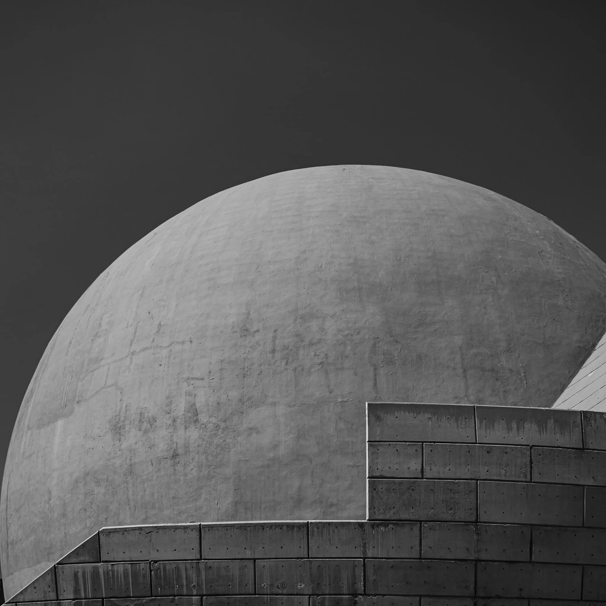 Black and white photo of a large, curved, concrete building, possibly a planetarium or observatory, with a darker sky in the background.