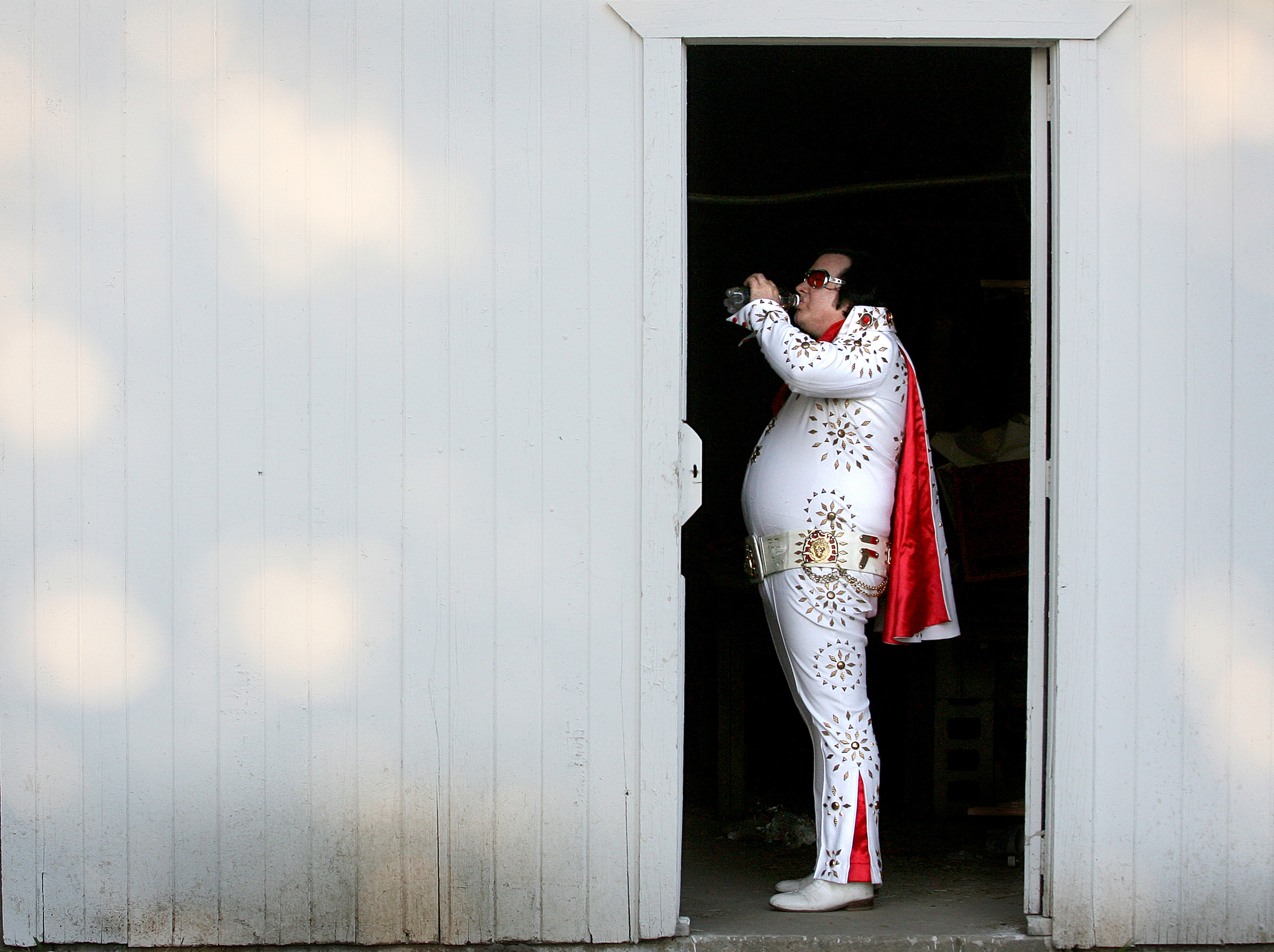 Known as Elvis Himselvis, Rick Dunham takes a swig of bottled water backstage before performing at the Clayton ball park in Clayton, Illinois during the 139th annual Adams/Brown County Old Settlers festival.