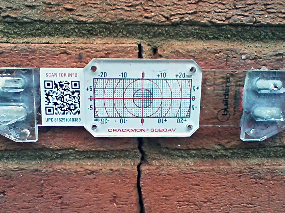 FIGURE 4. Buildera CRACKMON 5020AV crack monitor installed at position No. 2 between finished grade and third brick course along eastern wall. Initial crack width varies between 0.100 and 0.120 inches (2.54 to 3.05 mm). Inside caliper measurement reference: 4.587 inches.