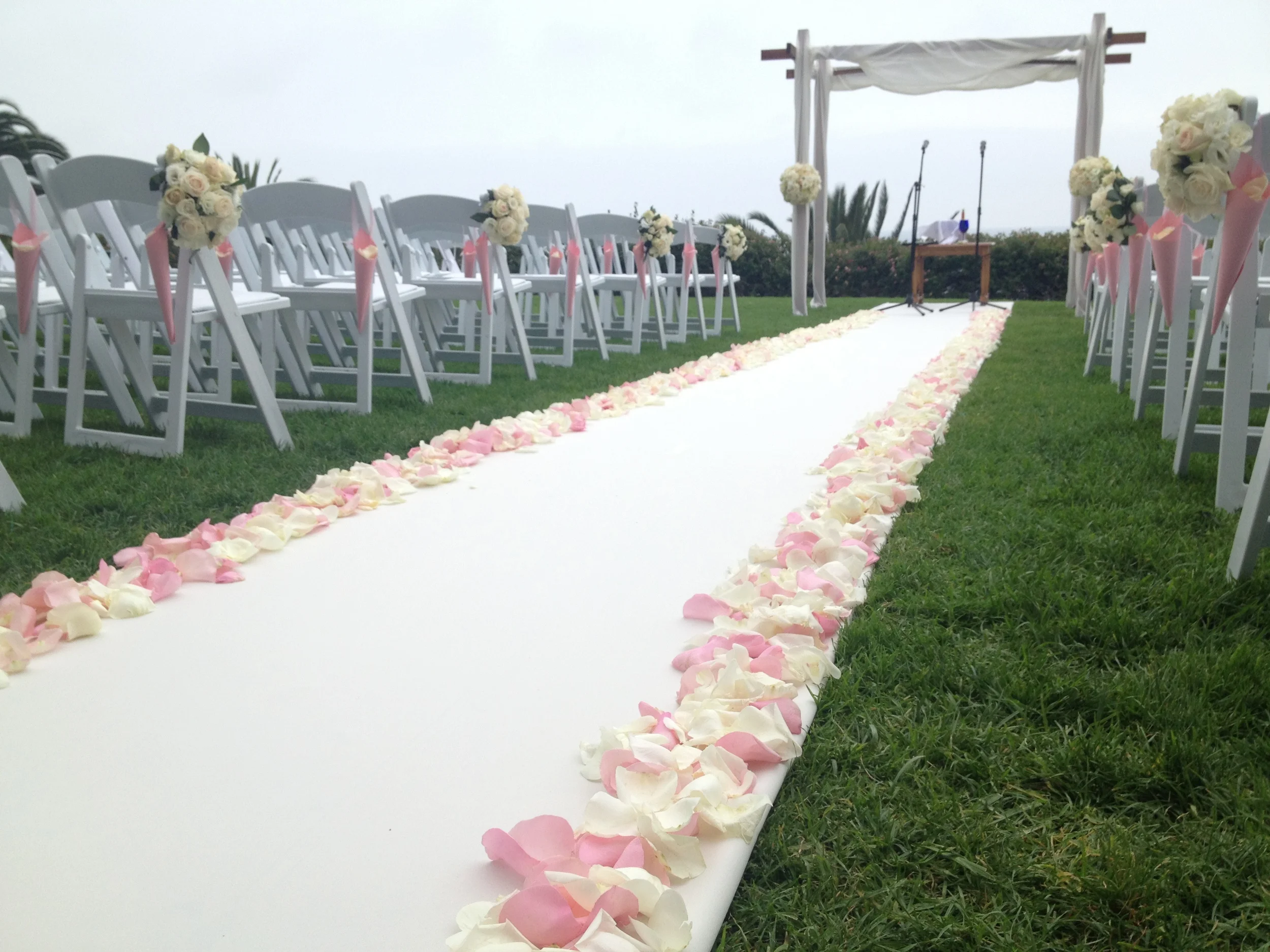 The completed ceremony site with Chuppah, aisle runner and petals, chair decor and paper cones filled with white roses petals. Now on to the reception.