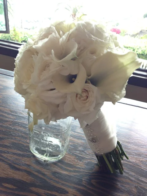 The Bridal bouquet made with garden roses, lisianthus, calla lilies, and ranunculus. The bouquet was wrapped in ivory satin ribbon with an overlay of mesh and embellished with pearl pins and rhinestone buttons. Lovely.