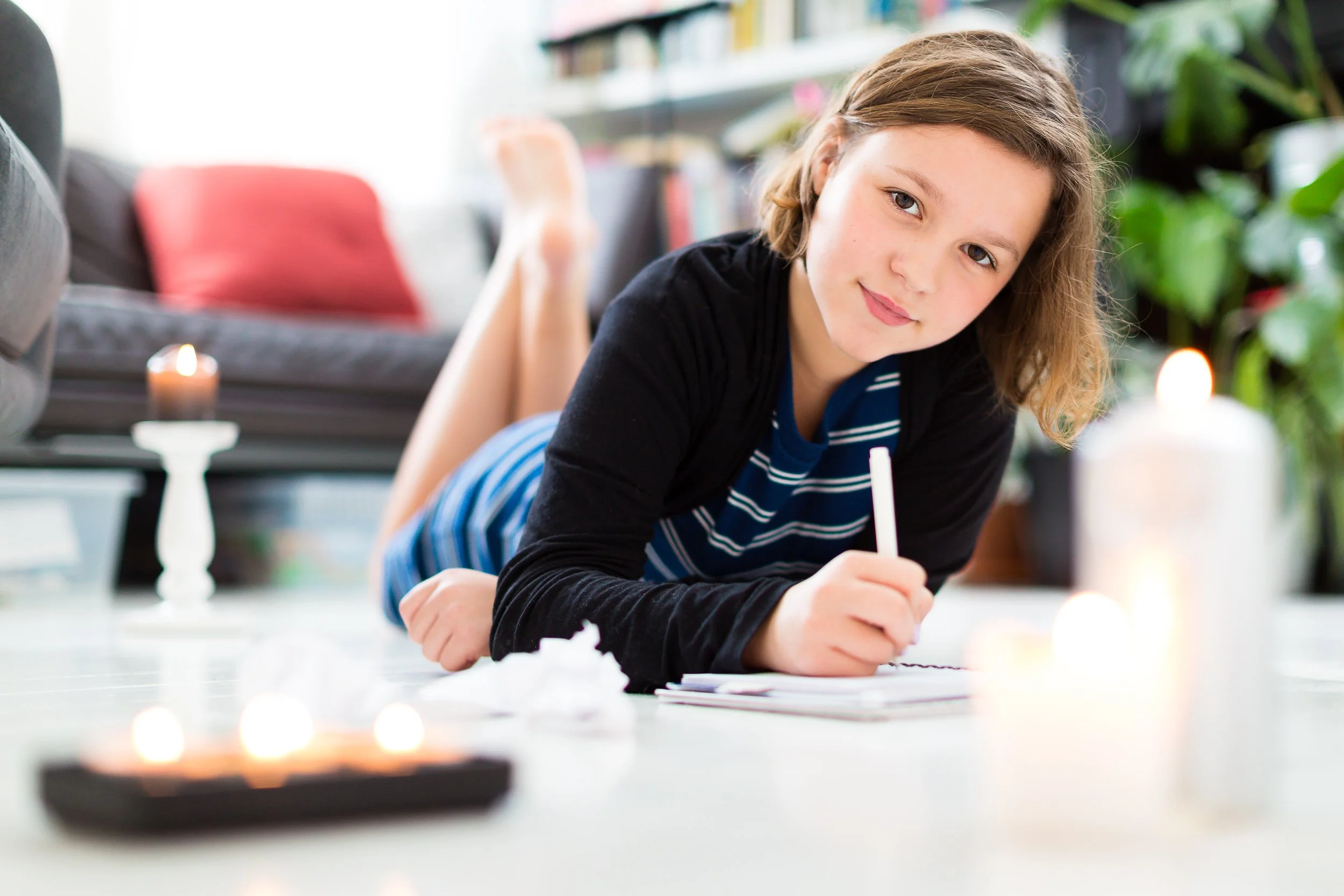 A young girl writes a letter while lying on her living room floor