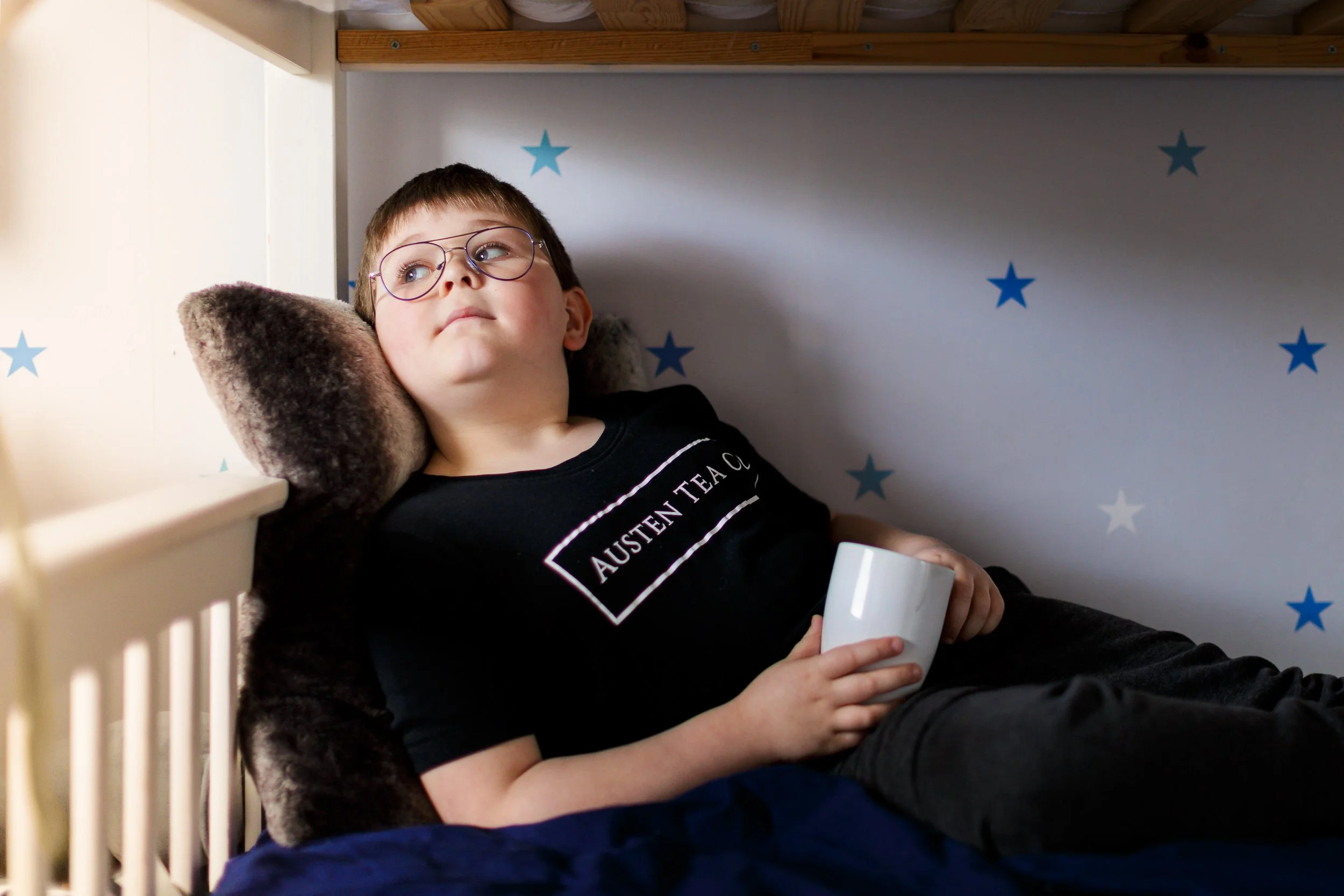 A boy lies in his bunk-bed holding a mug of tea