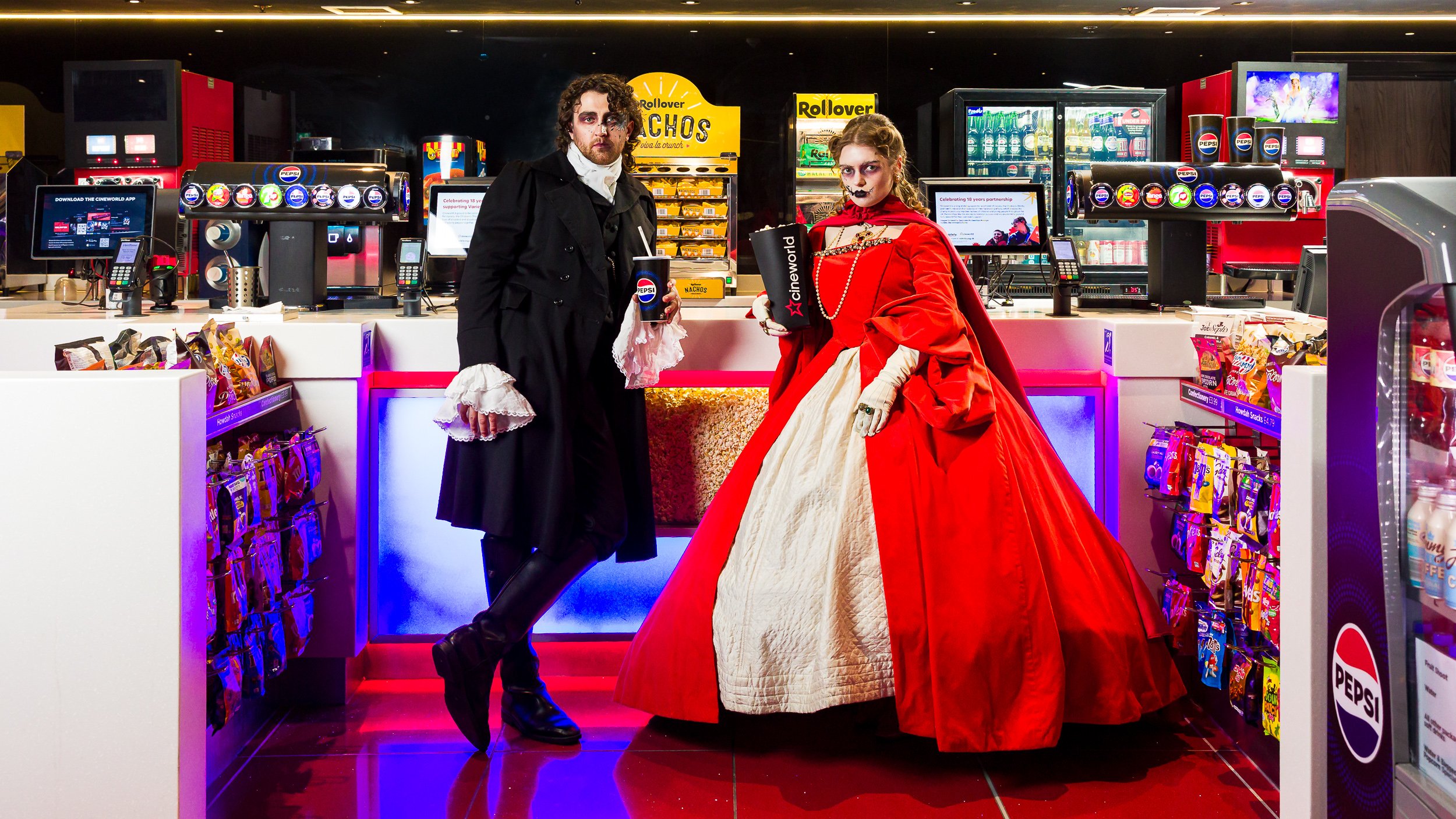 A man and woman in 18th century costume buying popcorn in the cinema