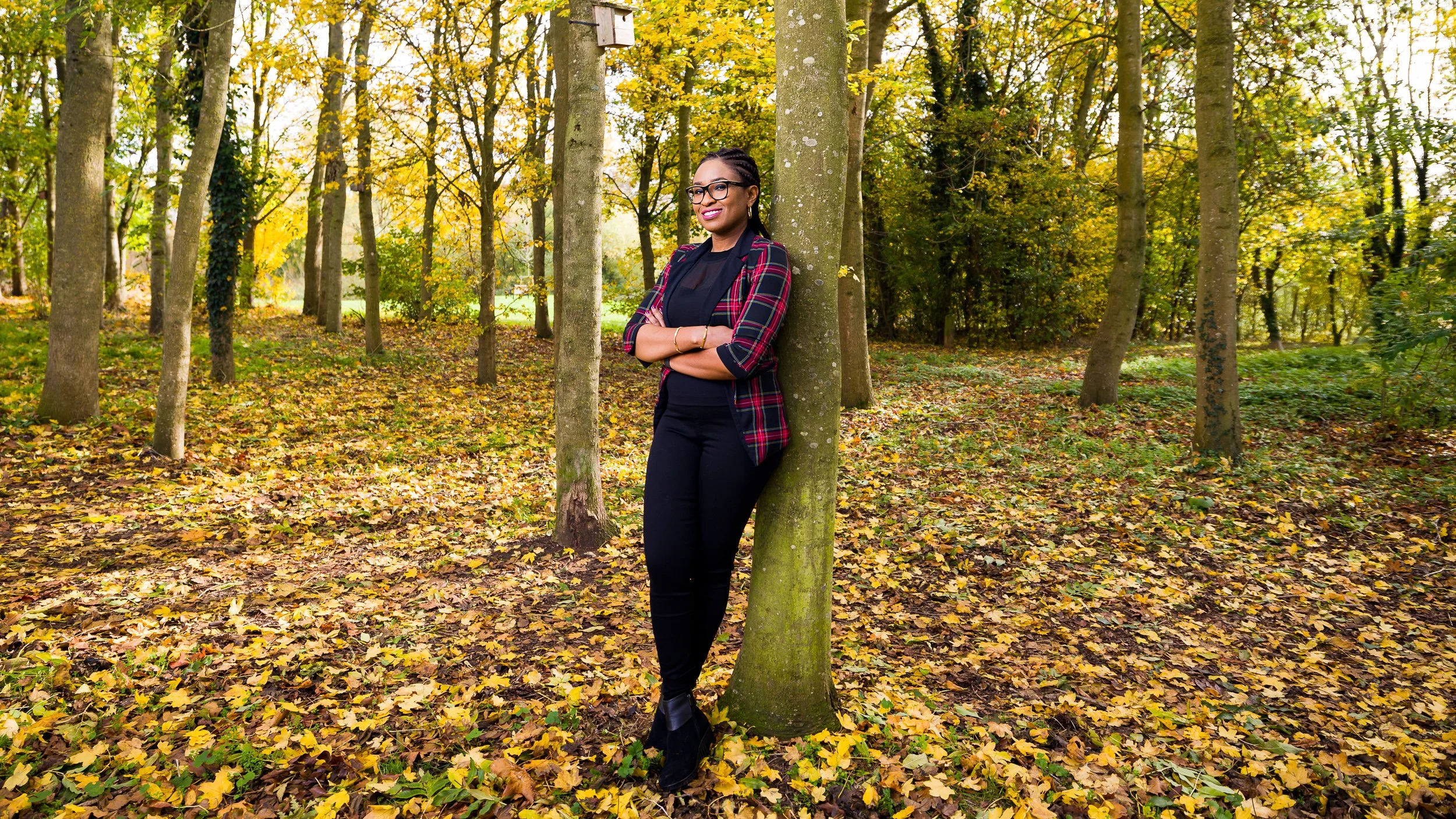 A woman leans against a tree in a wood