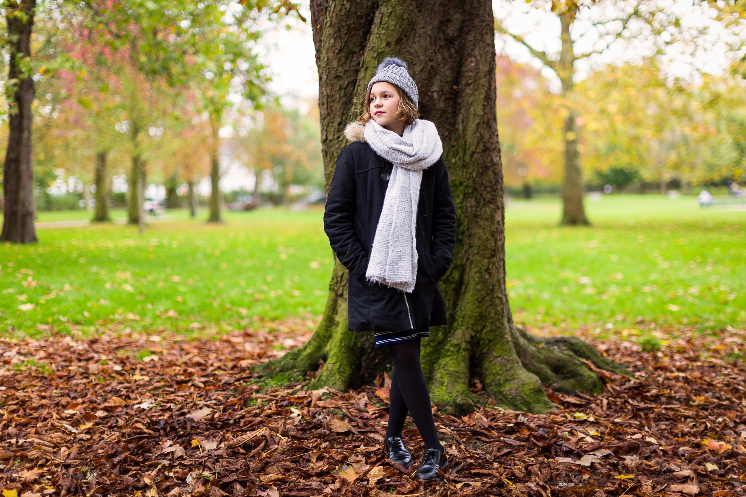 A young girl in a scarf standing outside in autumn looks away 