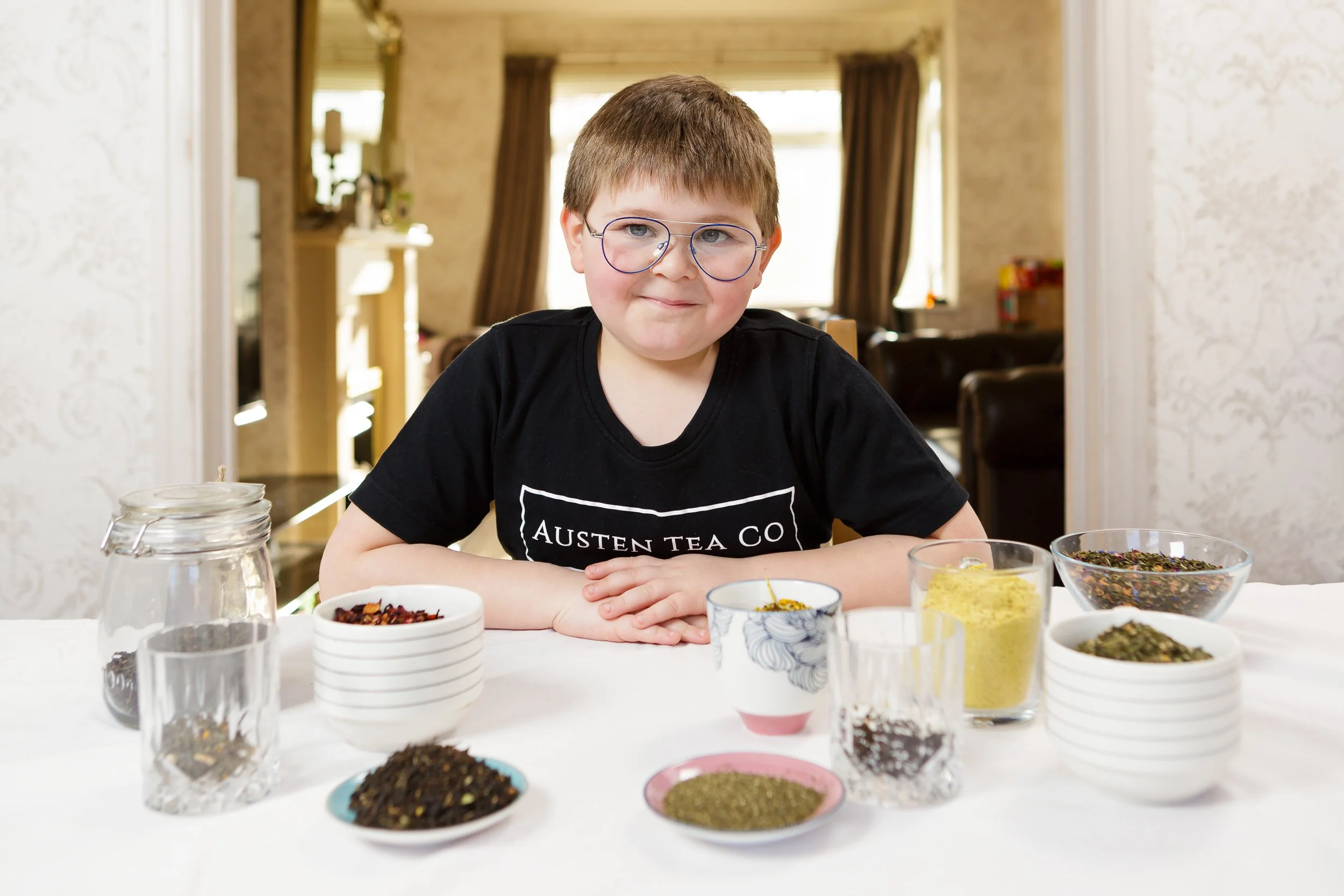 A boy sits proudly at his dining-room table in front of his different kinds of tea 
