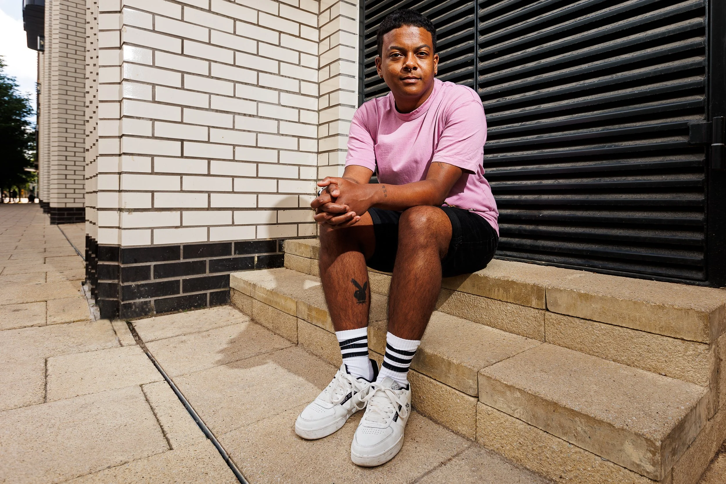 A young man in a pink shirt sits on a step